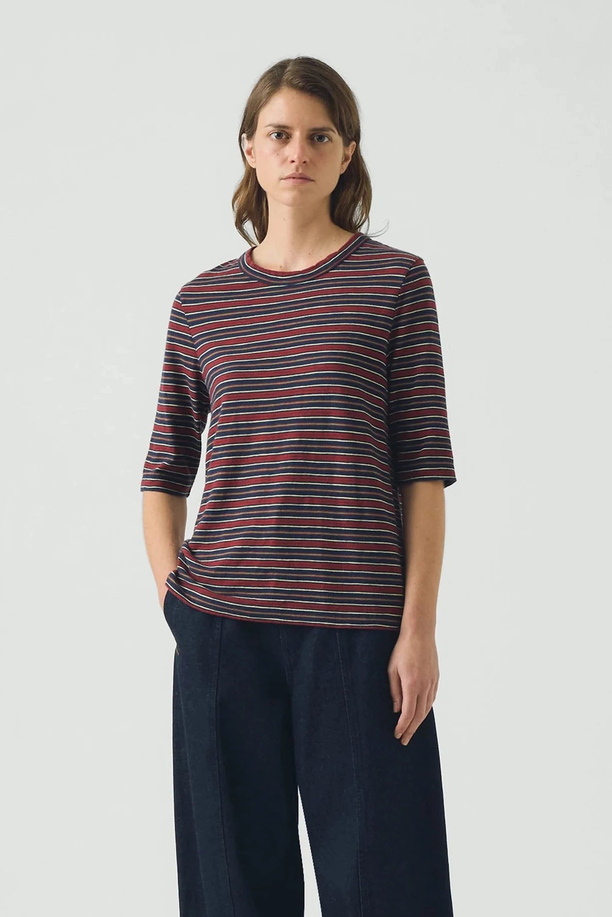 Woman wearing a striped shirt and dark pants against a plain background