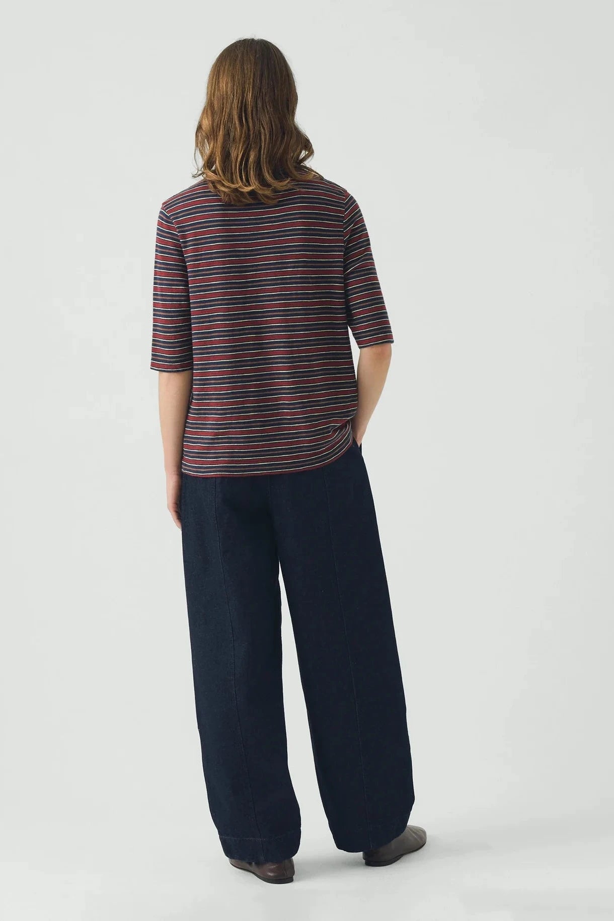 Person wearing a striped shirt and dark pants on a white background
