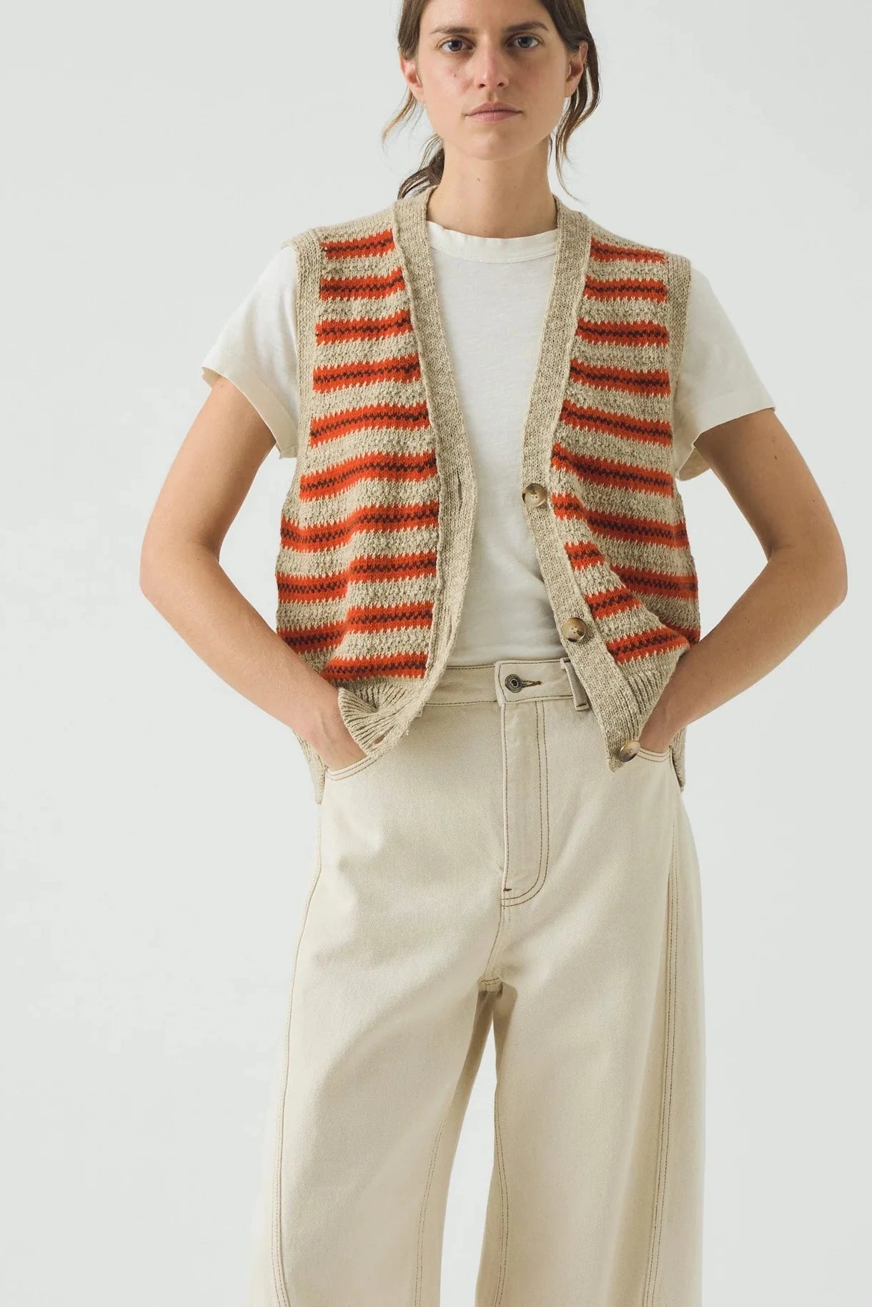 Person wearing a striped vest over a white shirt with beige pants on a plain background