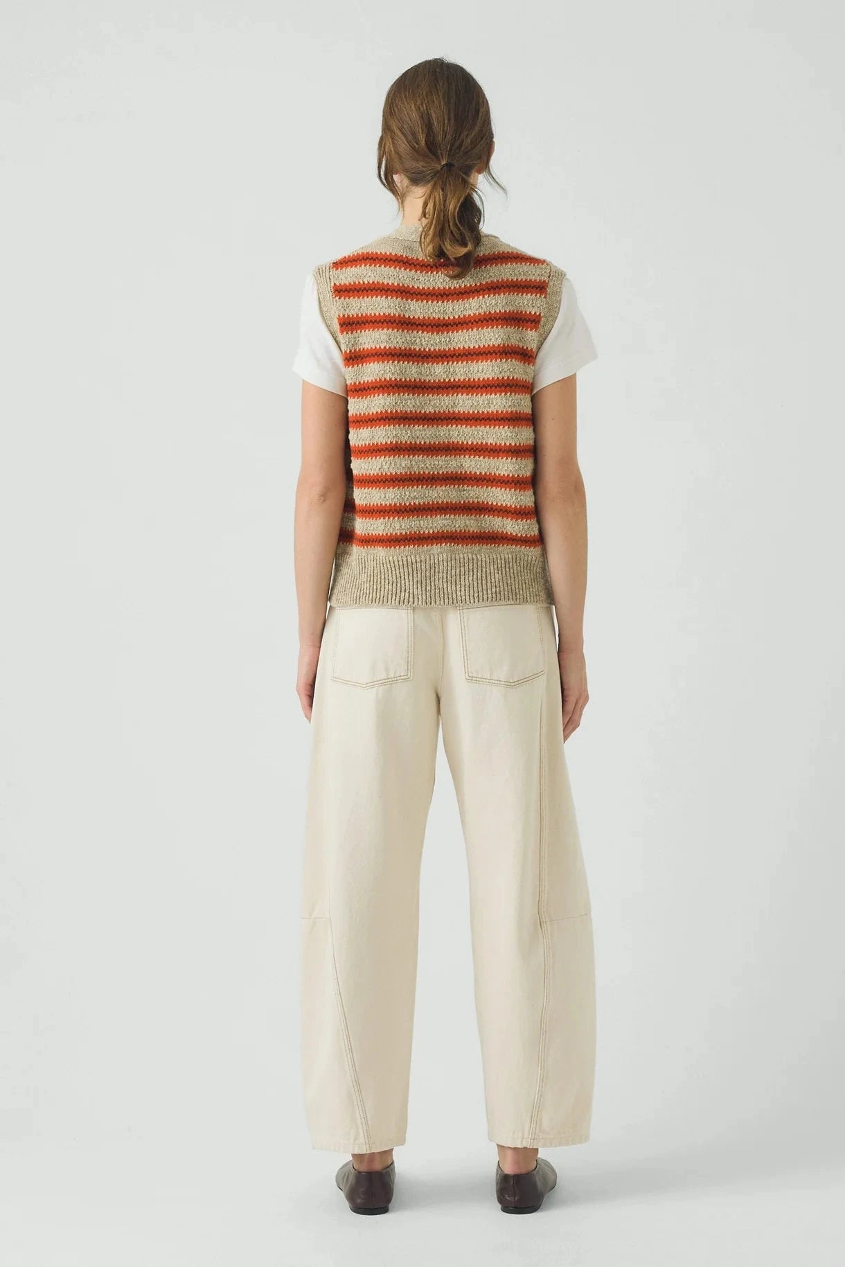 Person wearing a striped sleeveless top and beige pants on a white background