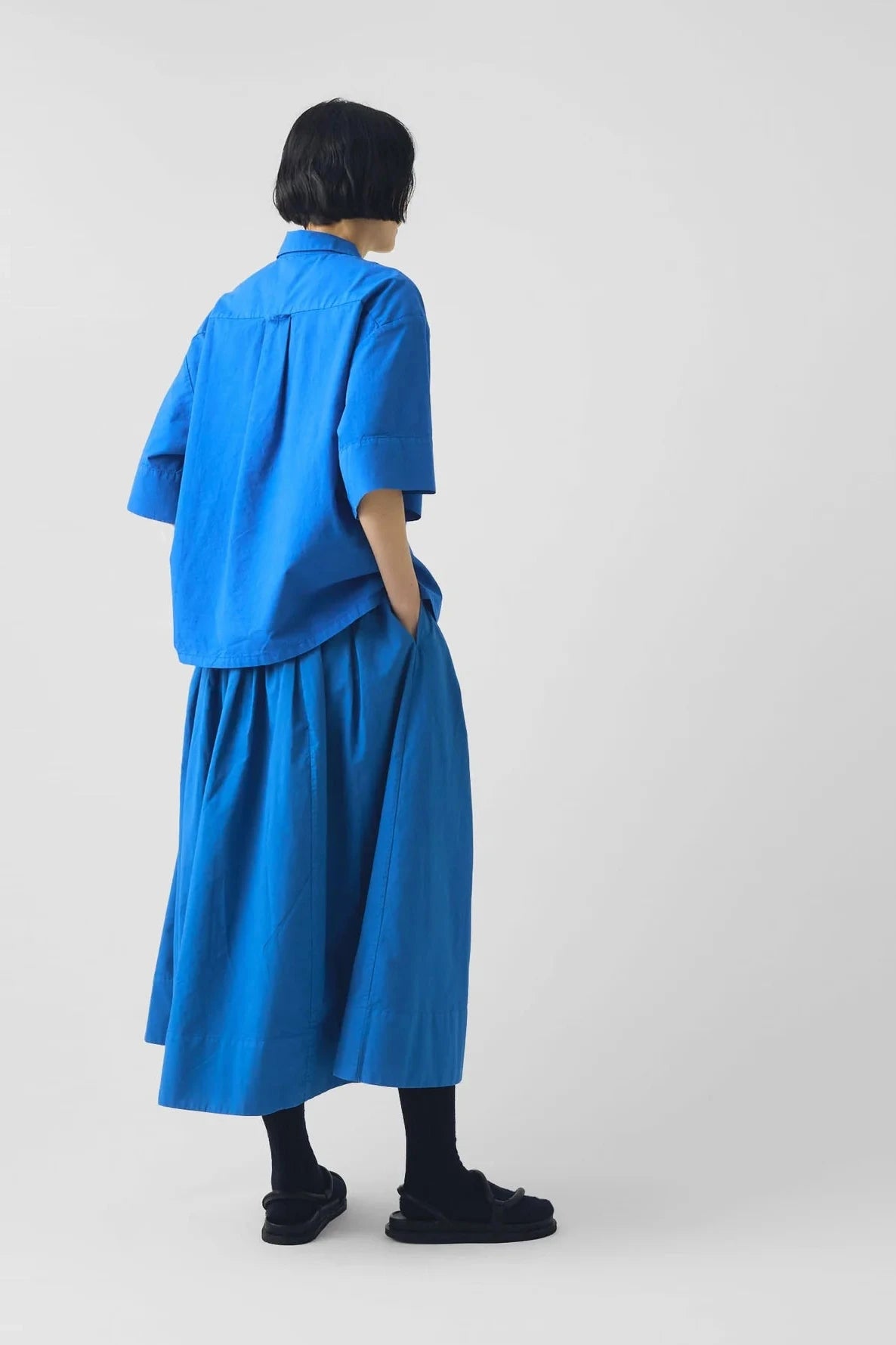Person wearing a blue shirt and skirt standing against a white background