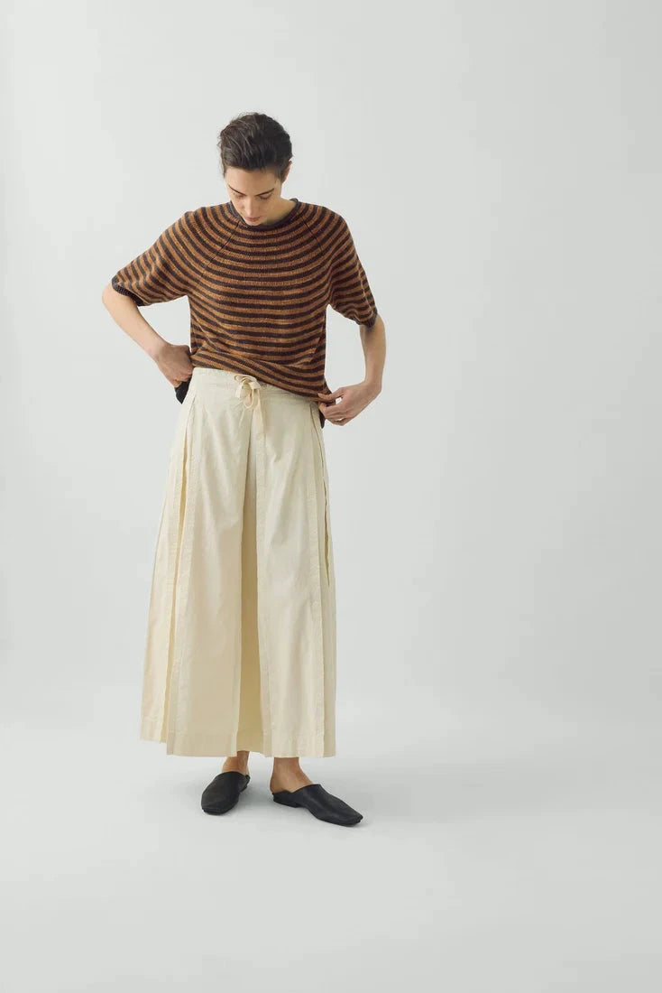 Full length view of the voluminous ecru TOAST skirt in motion, grounded by simple black slides
