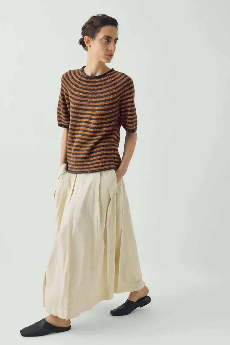 Full length view of the voluminous ecru TOAST skirt in motion, grounded by simple black slides