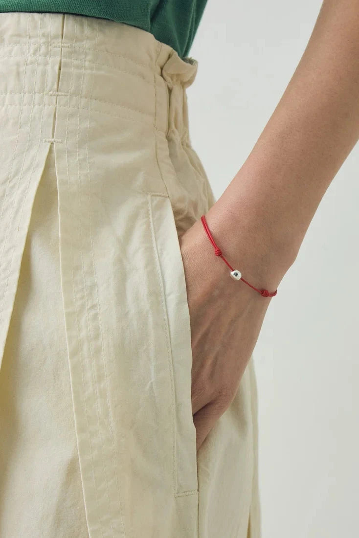 Close up detail of the structured box pleat and utility pocket on the TOAST ecru skirt with a hand in pocket and red bracelet