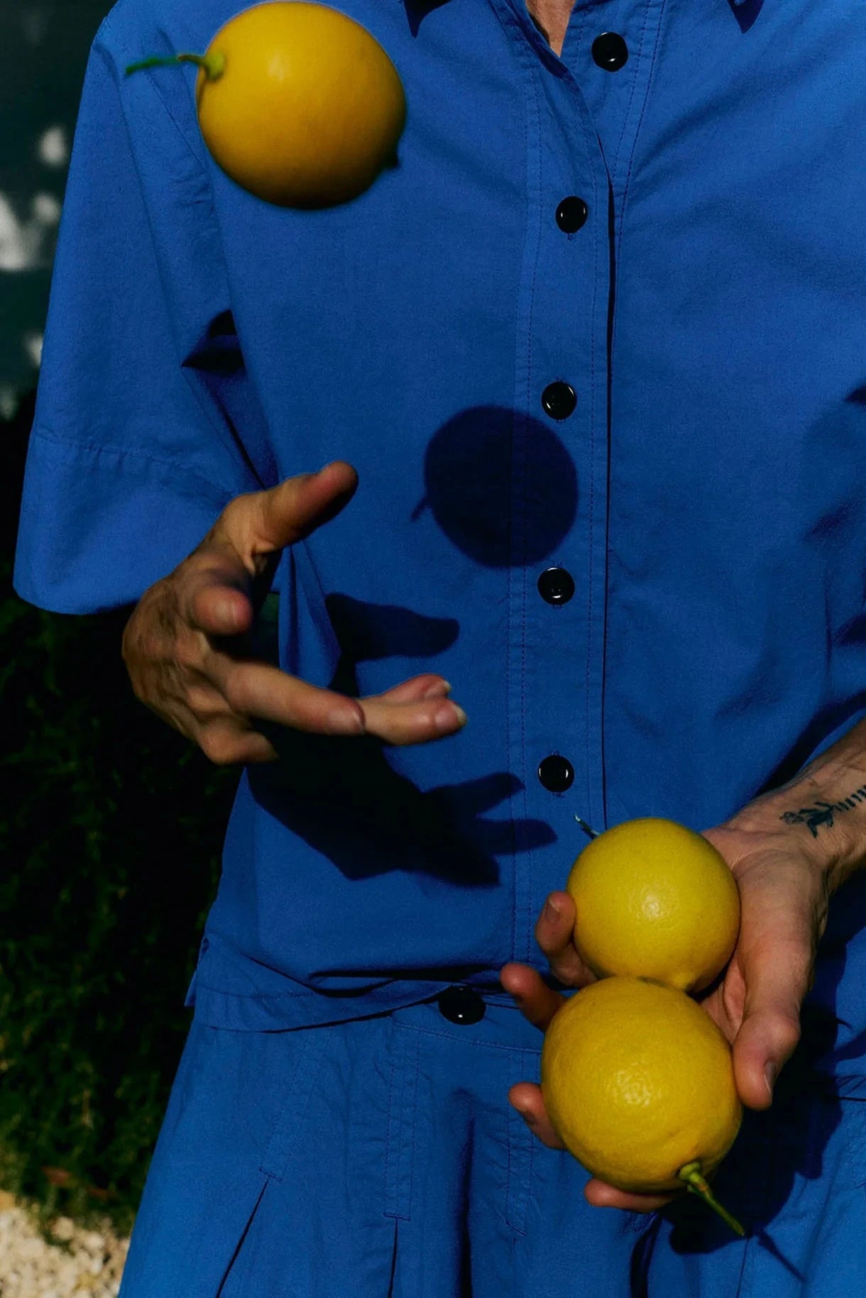 Person wearing a blue outfit juggling  two lemons with a blurred background