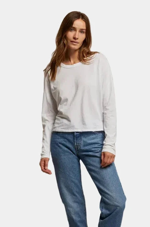 Woman wearing a white long-sleeve shirt and blue jeans against a plain background
