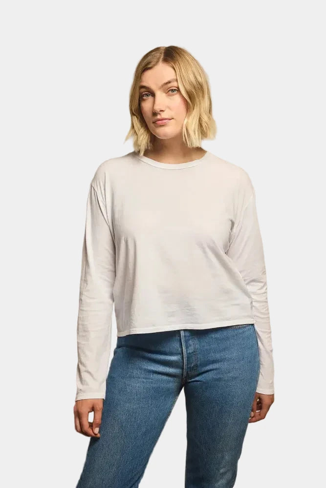 Woman wearing a white long-sleeve top and blue jeans against a beige background