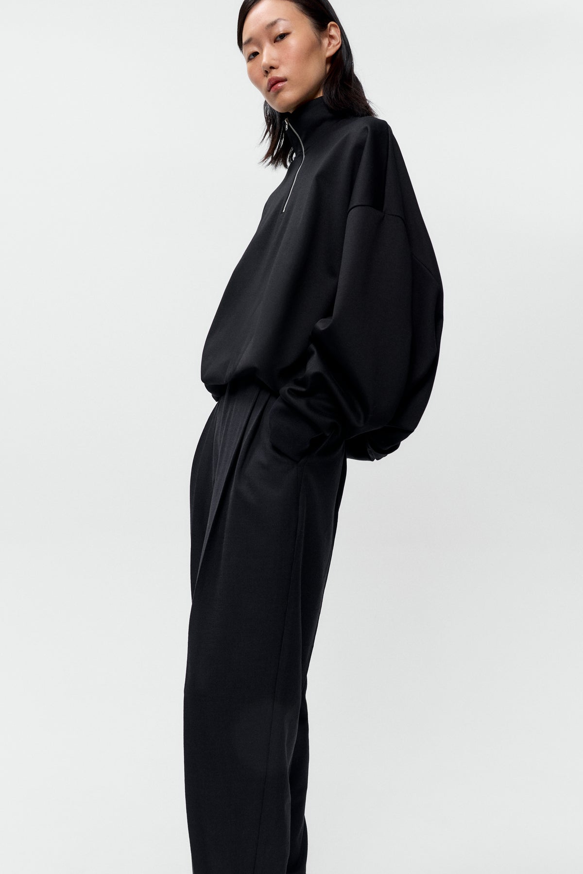 Side view of model wearing Cordera black balloon quarter zip pullover with silver hardware - East Coast General