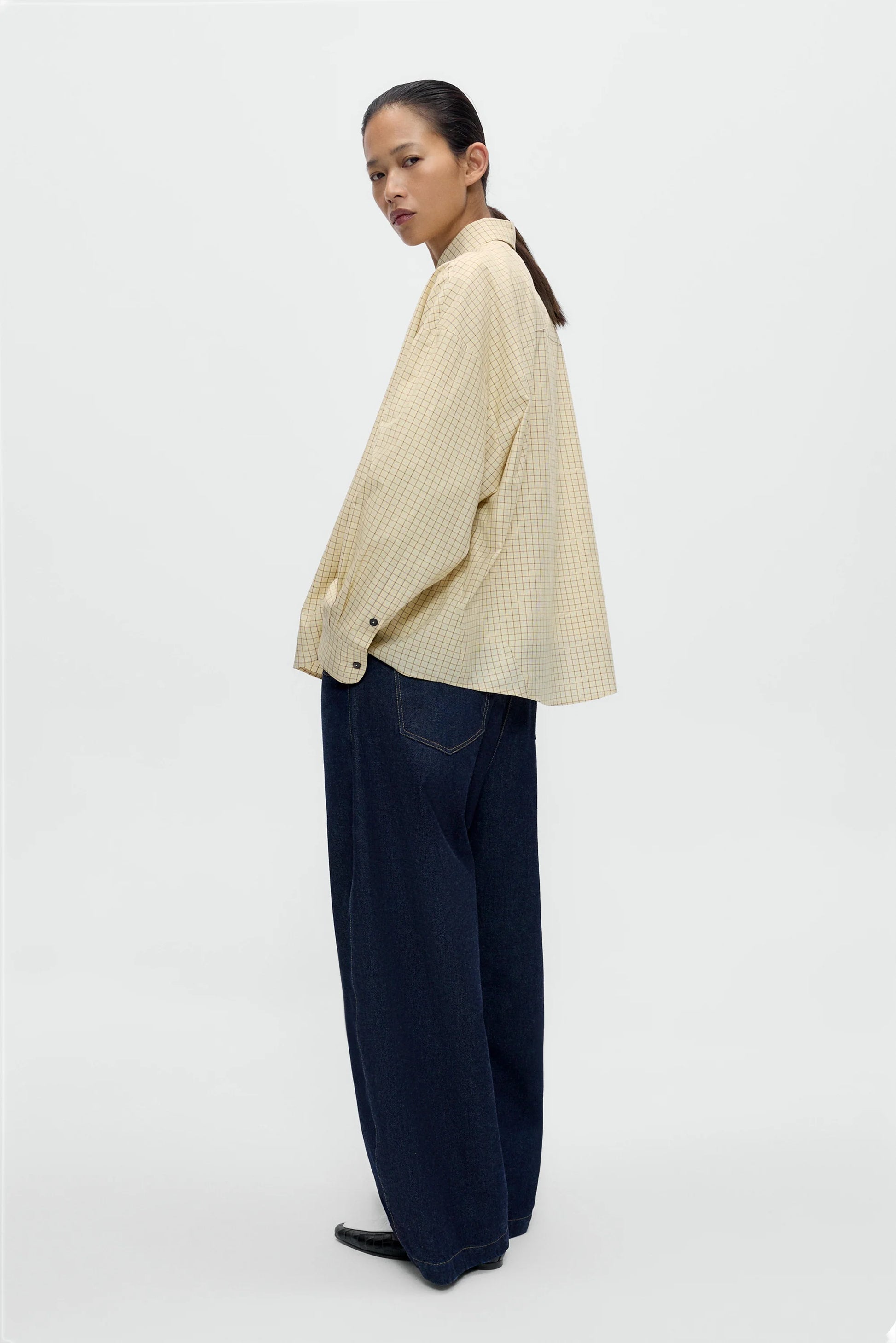 Woman wearing a beige shirt and dark pants on a white background