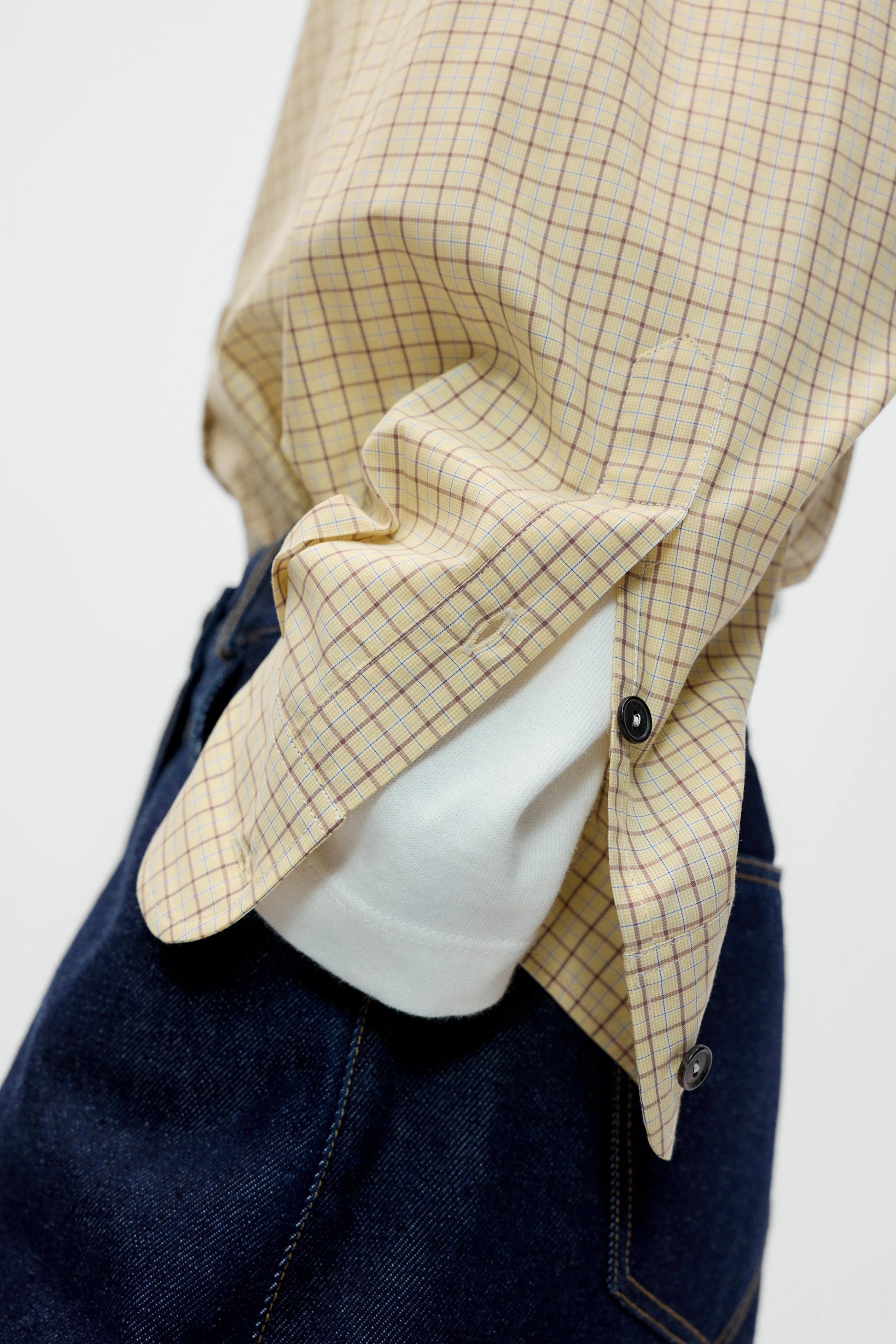 Detailed close up of a shirt cuff with white long sleeve underneath, styled with navy blue jeans