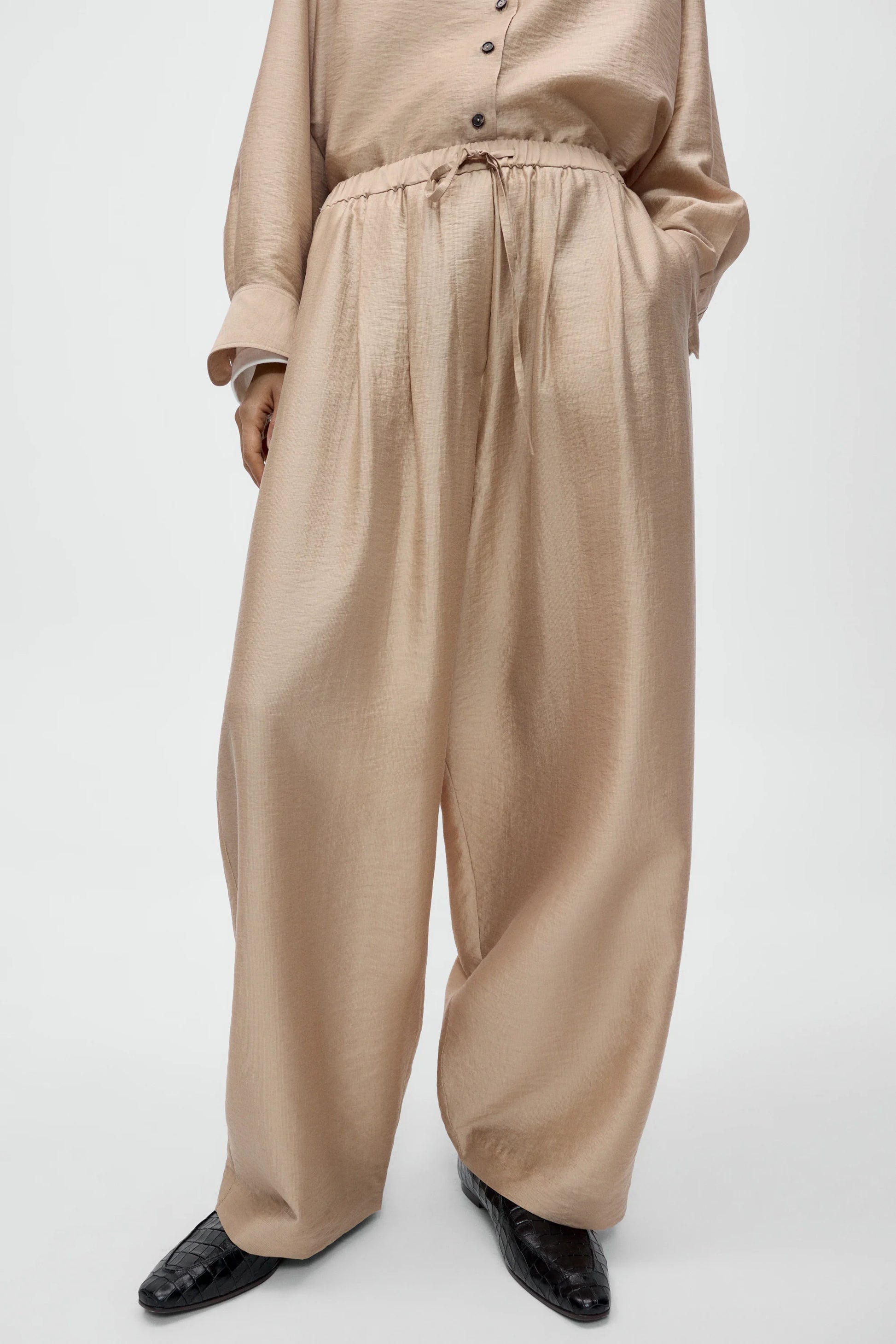 Beige pants worn with a beige shirt on a white background