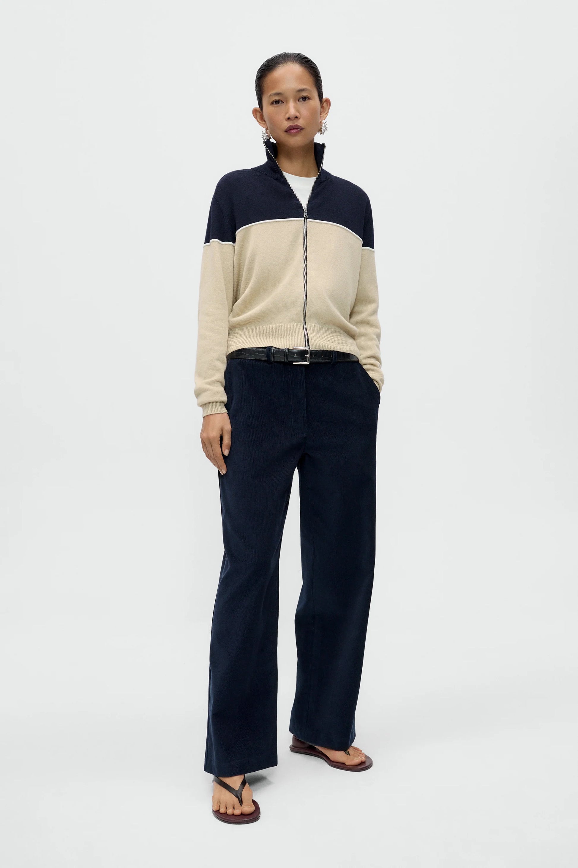 a lady wearing a navy and cream zip through cardigan and navy trousers against a white background