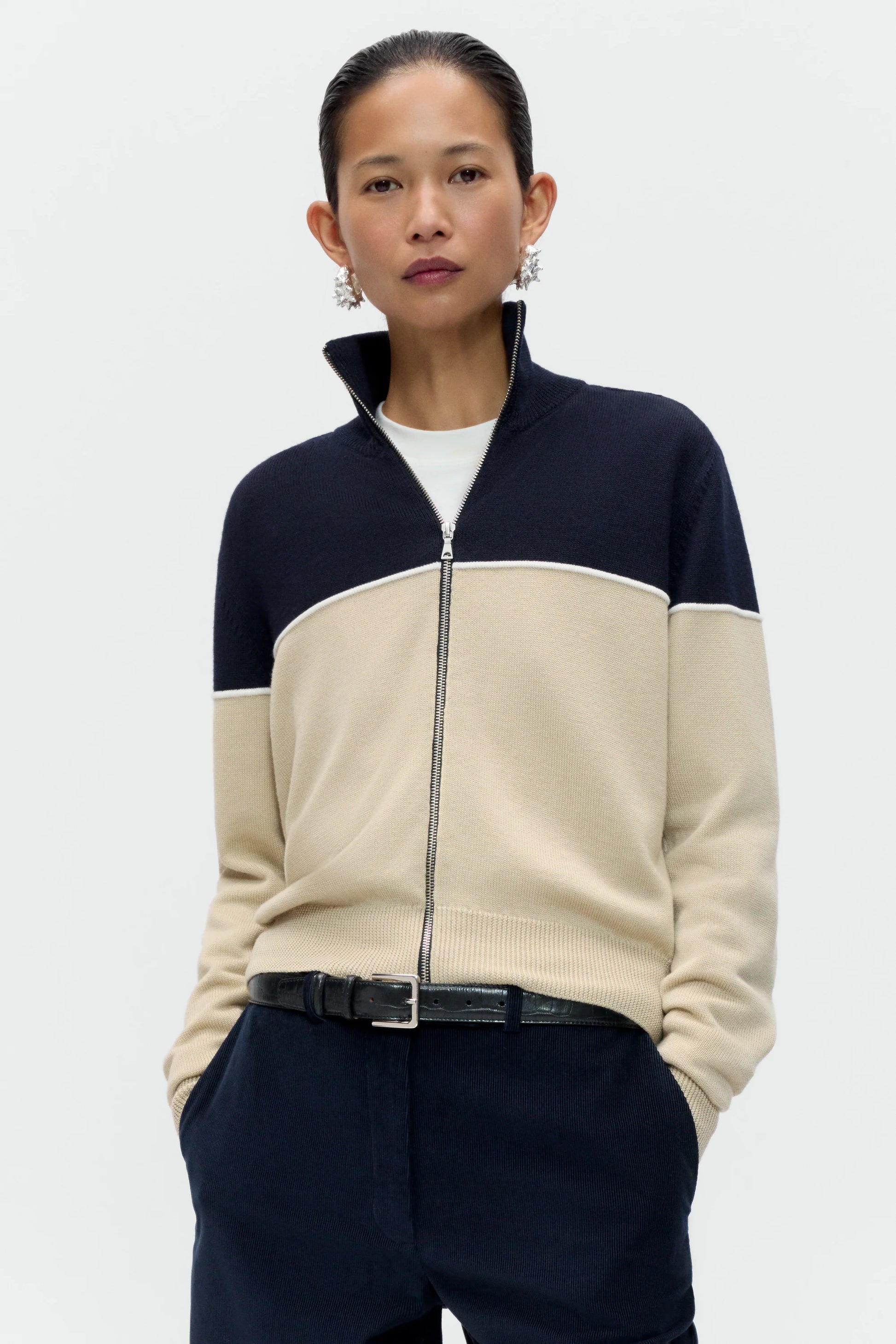 a lady wearing a blue and cream zip through cardigan and navy pants against a white background