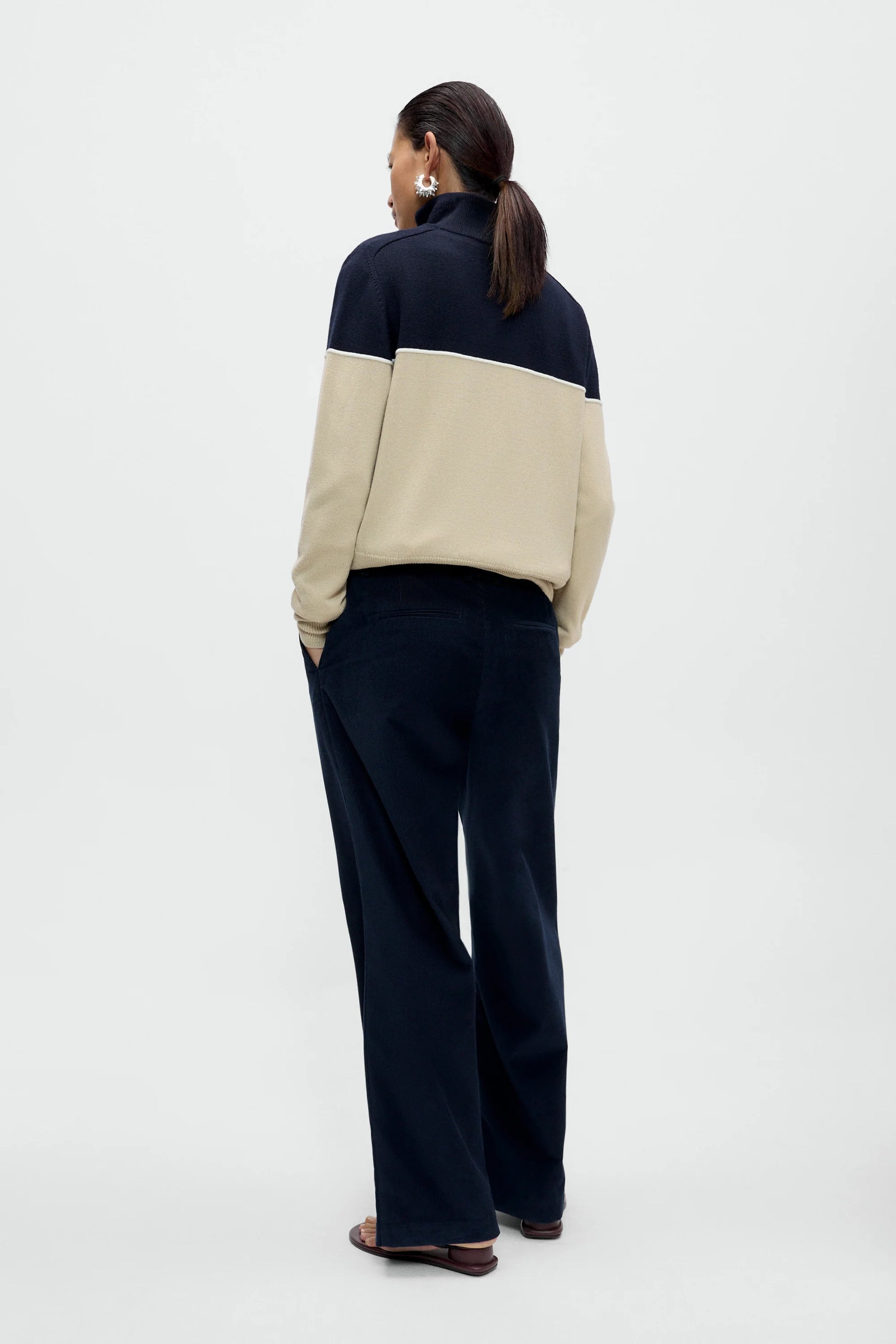 a women wearing a navy and cream cardigan with navy pants against a white background. Viewed from the back