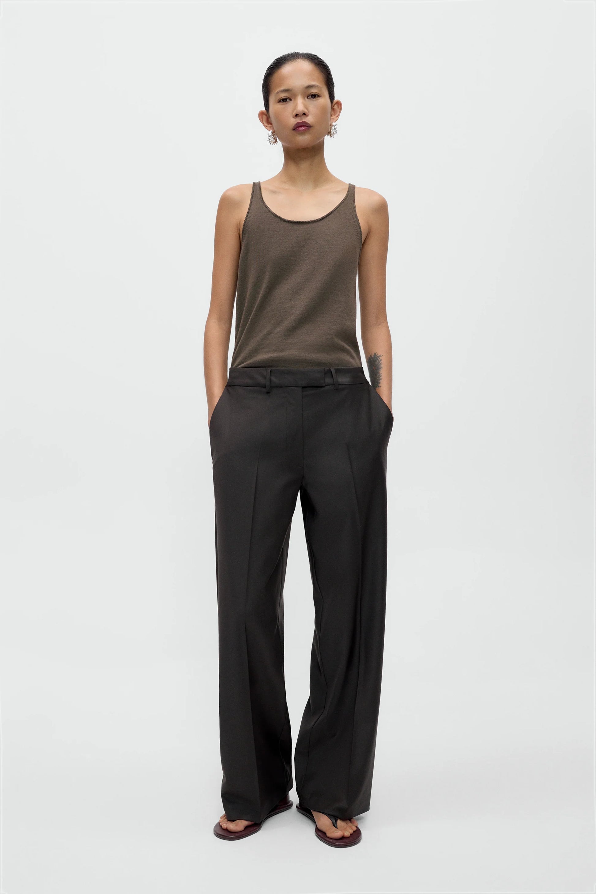 Woman wearing a brown tank top and black pants on a white background