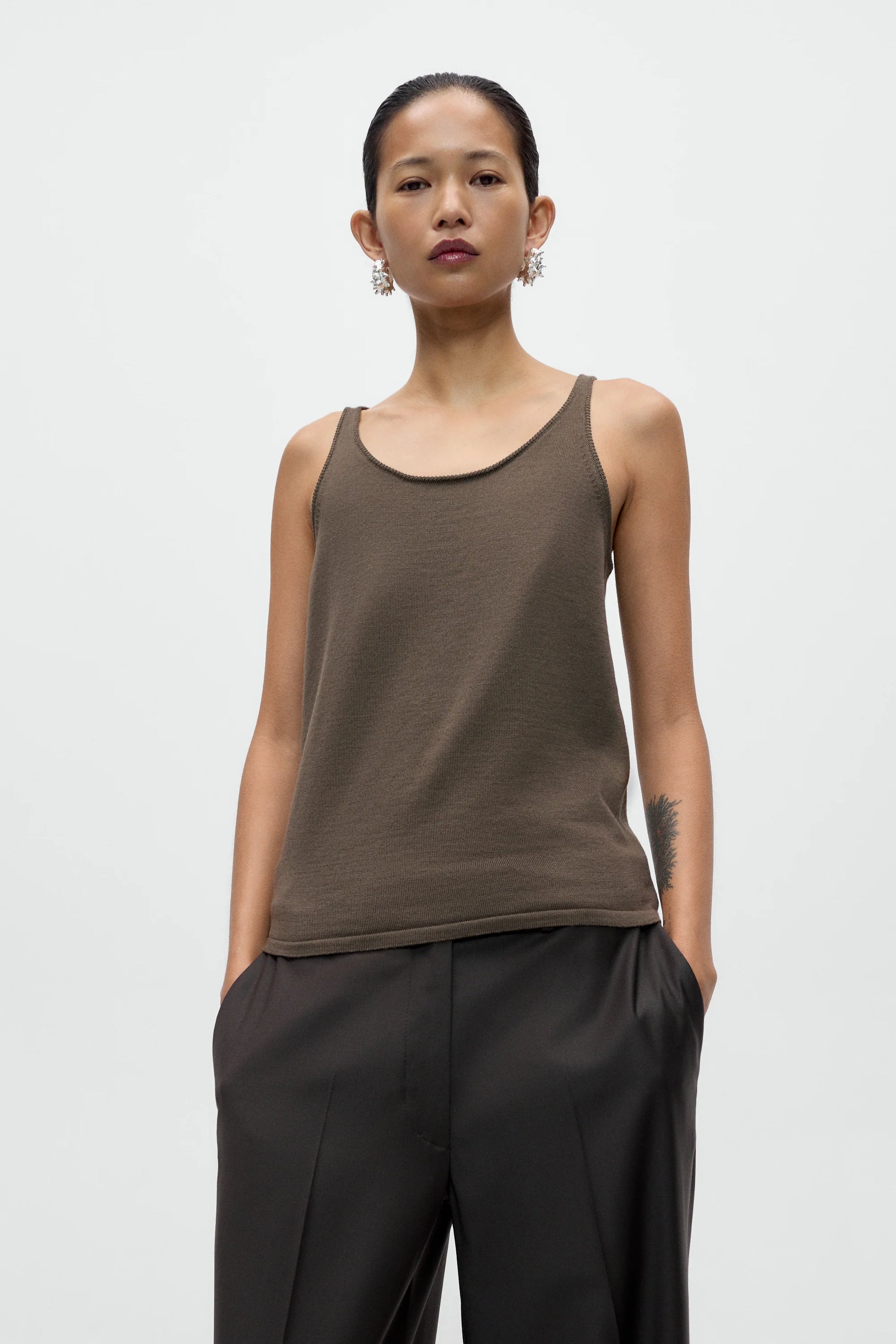 Woman wearing a brown tank top and black pants against a white background