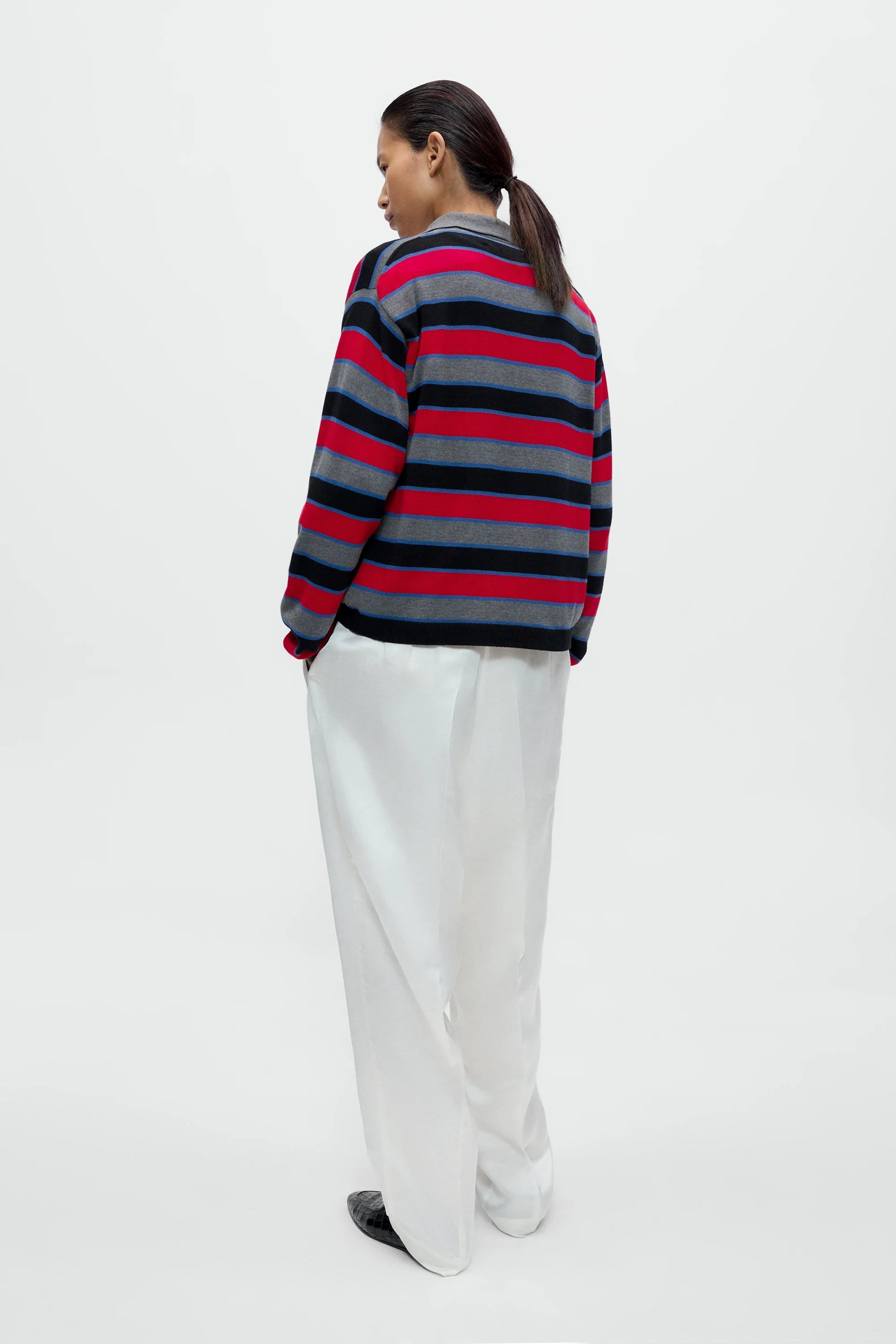 Person wearing a striped sweater and white pants on a white background