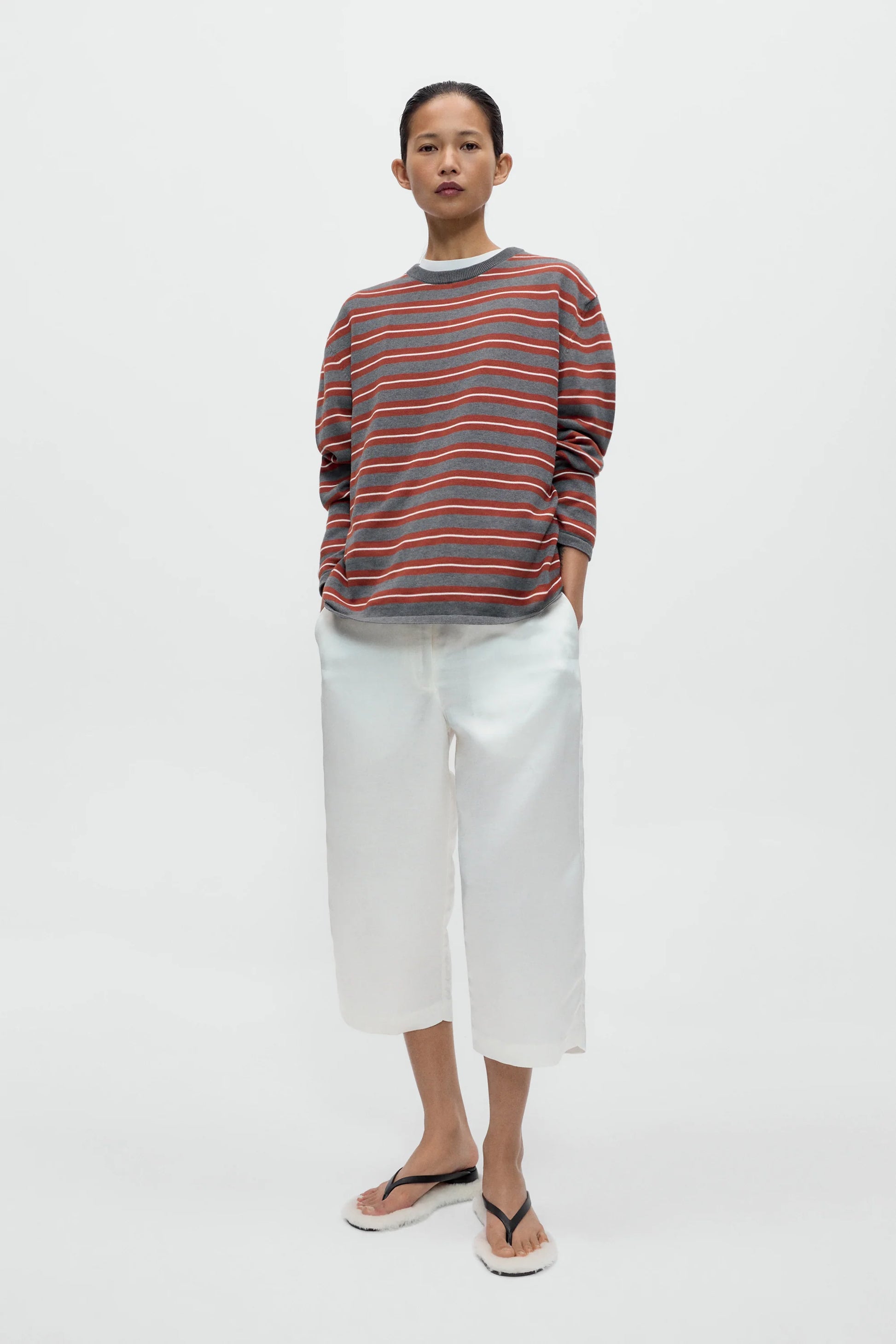 Person wearing a striped sweater and white pants on a plain background