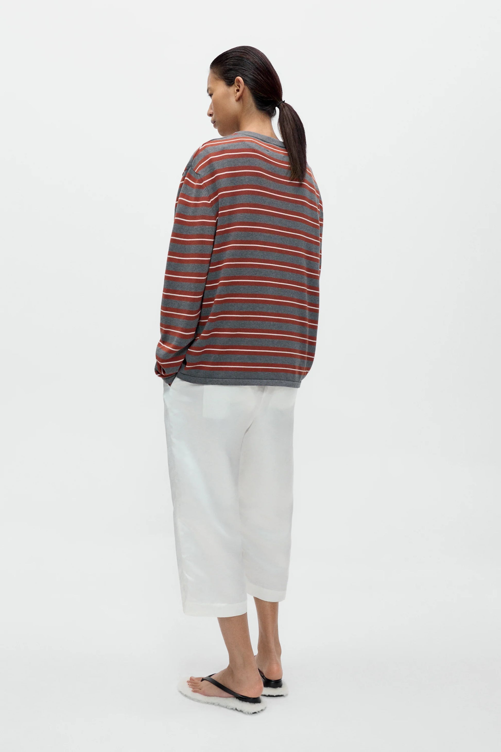 Person wearing a striped sweater and white pants on a white background