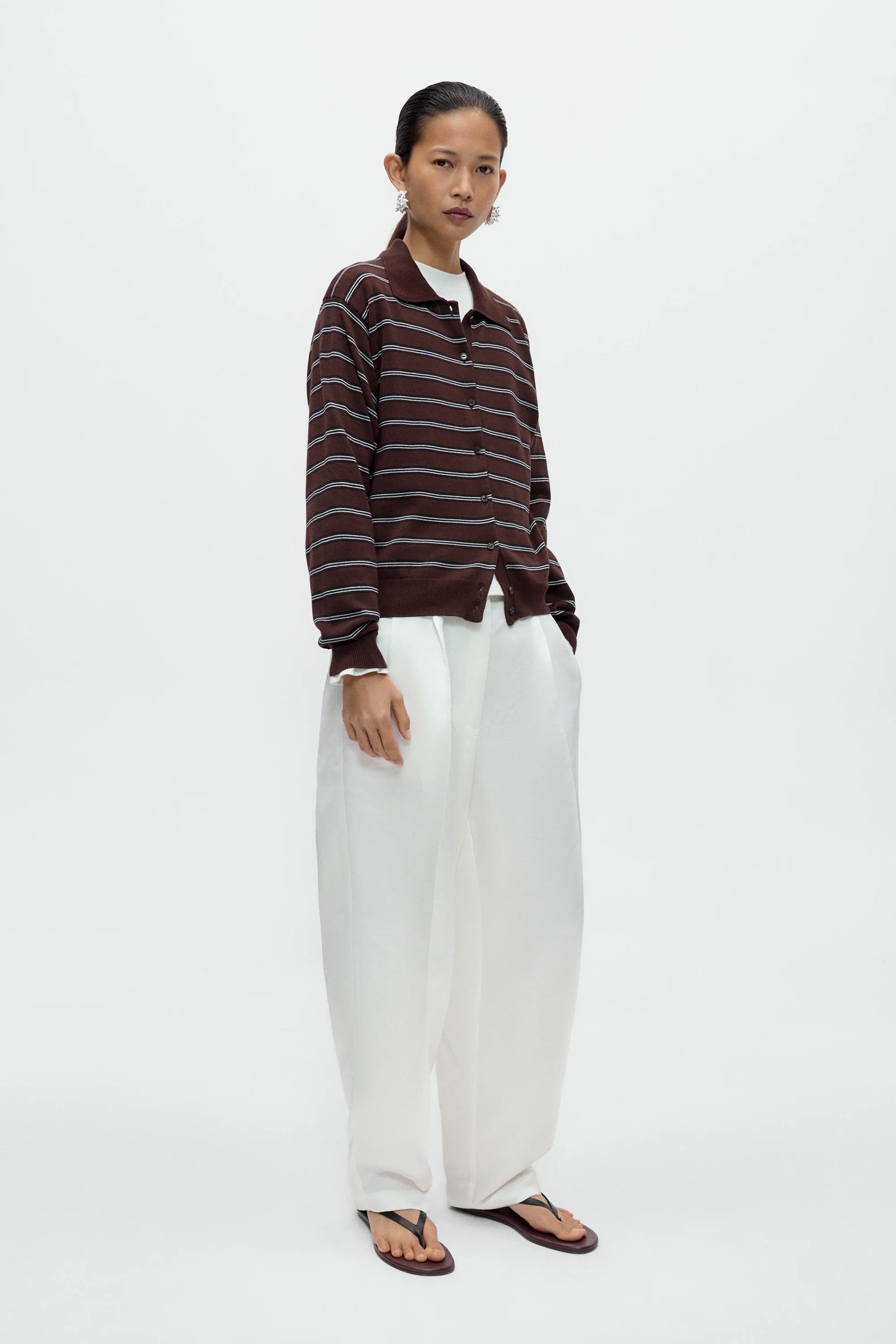 Person wearing a brown striped sweater and white pants on a white background