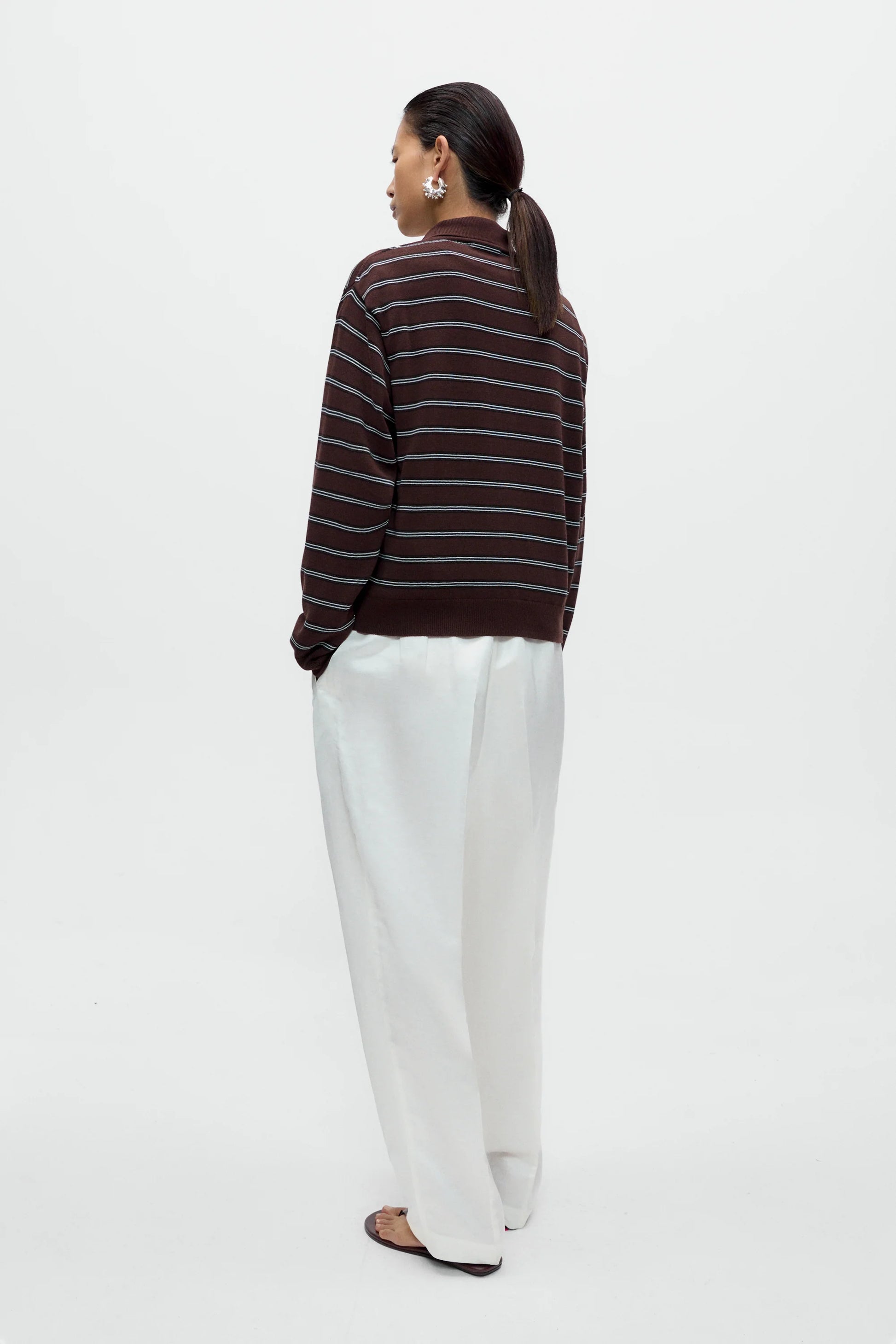 Person wearing a striped sweater and white pants on a white background