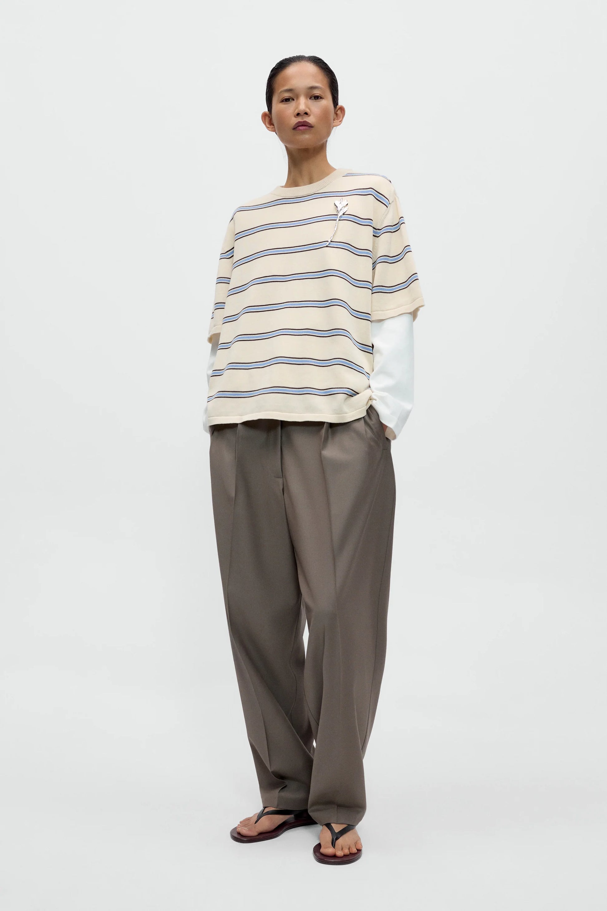 Person wearing a striped shirt and beige pants on a white background
