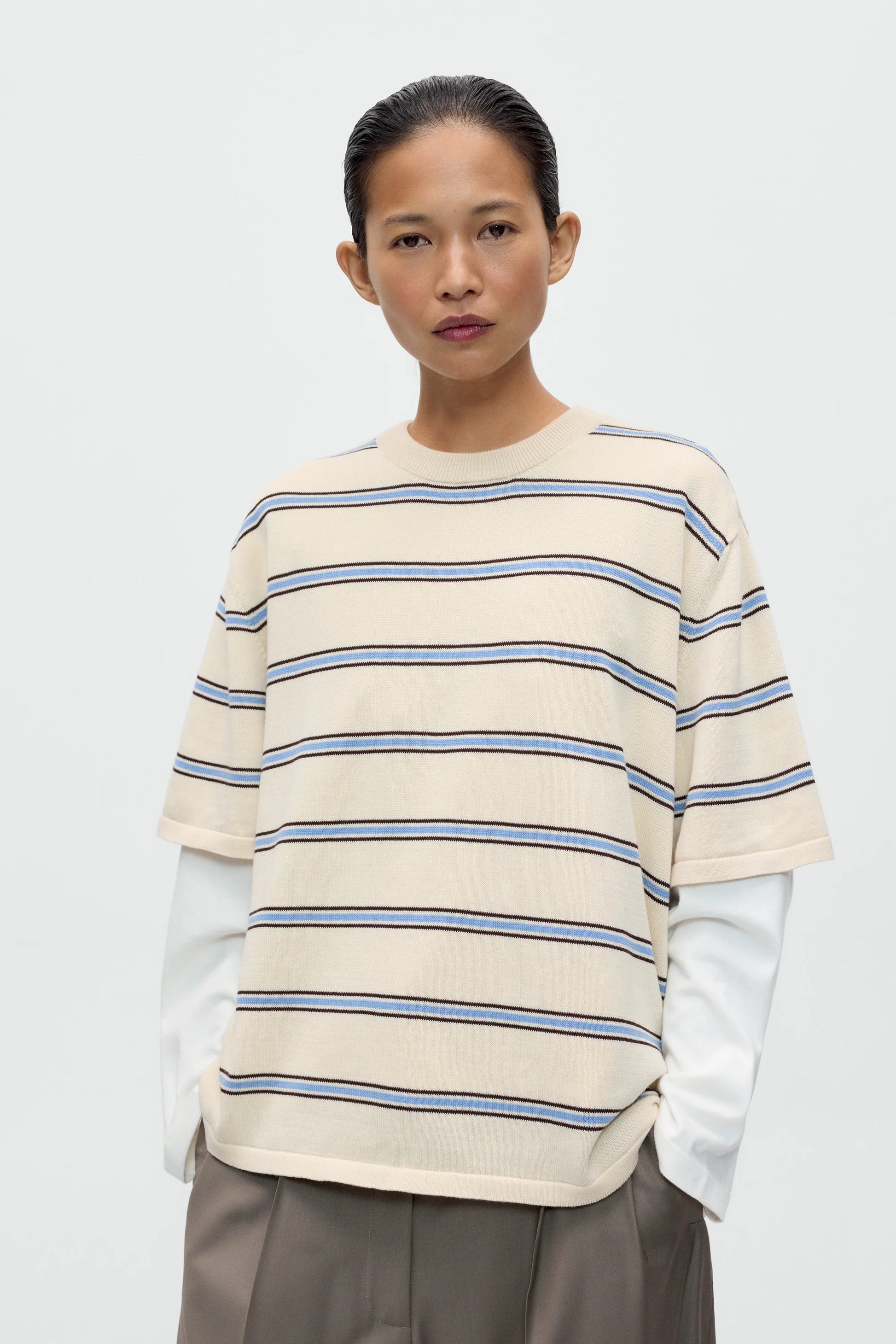 Person wearing a cream and blue striped sweater with a plain background