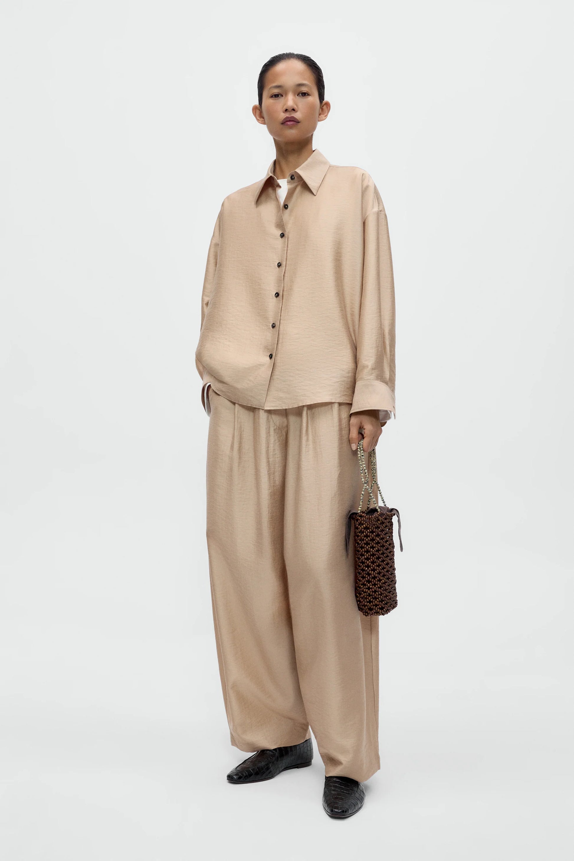 Person wearing a beige outfit holding a patterned handbag on a white background