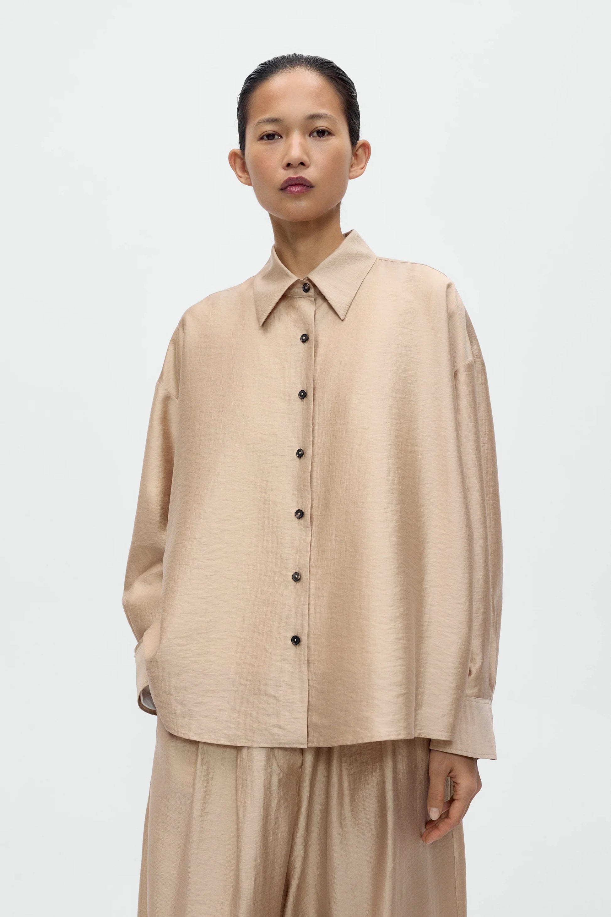 Woman wearing a beige button-up shirt and pants on a white background