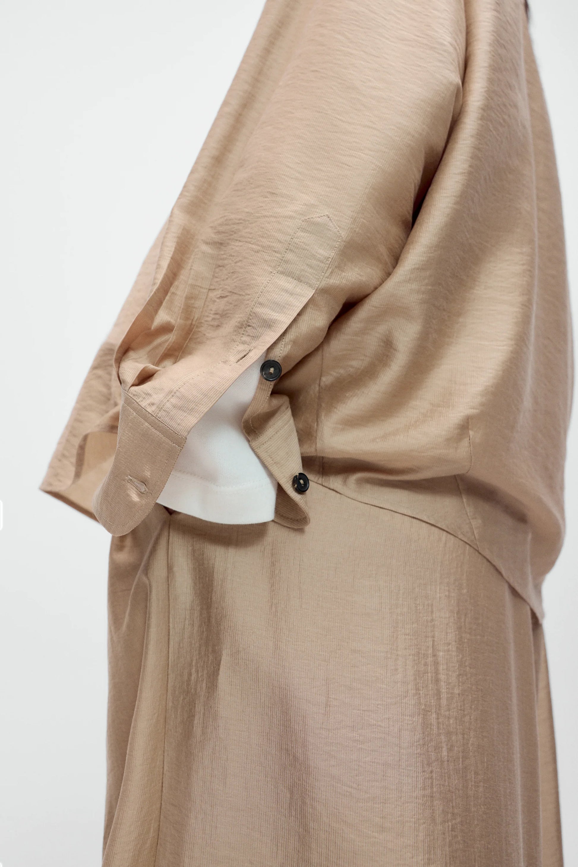 Beige outfit with a white shirt underneath on a plain background