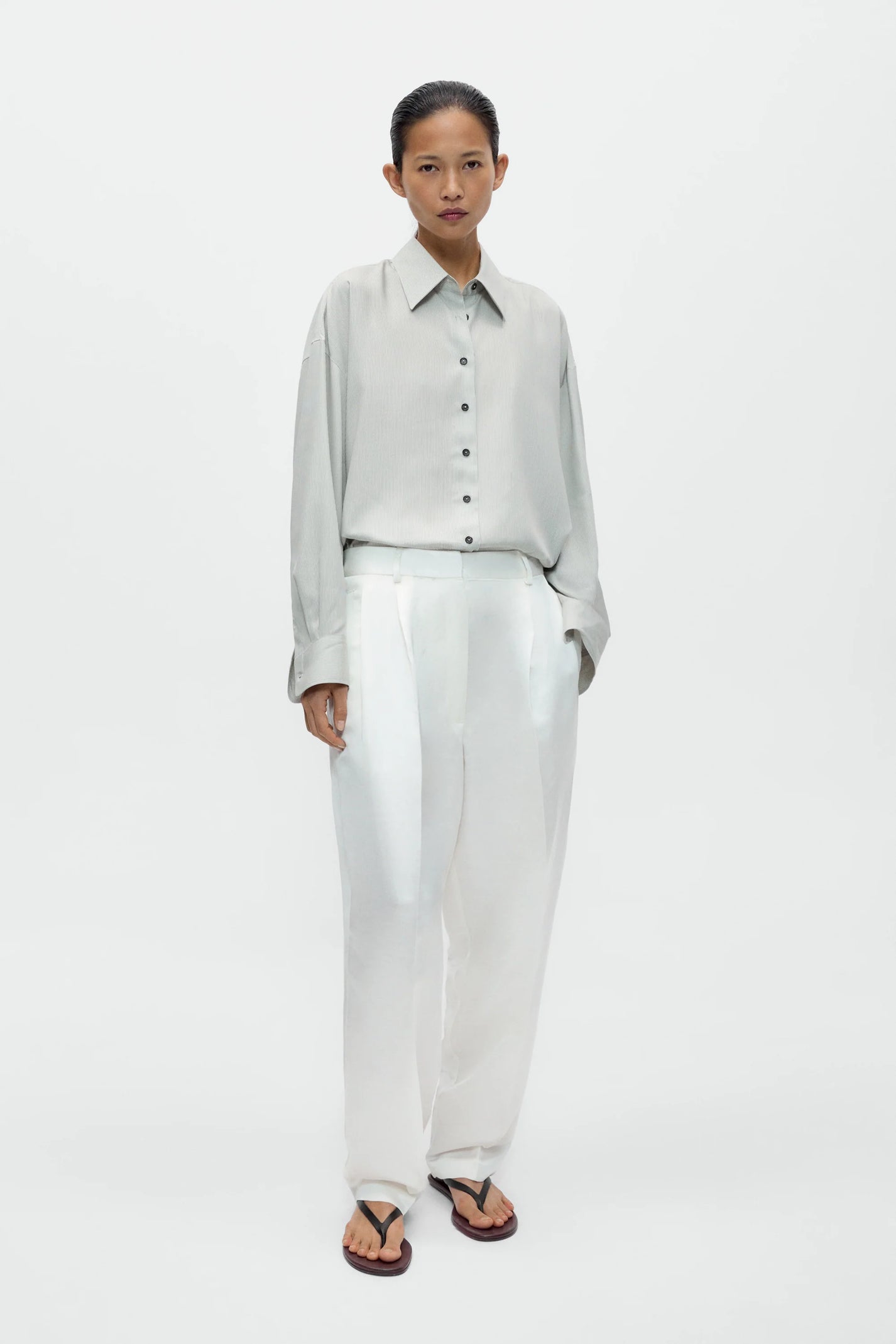 Woman wearing a light gray shirt and white pants on a white background