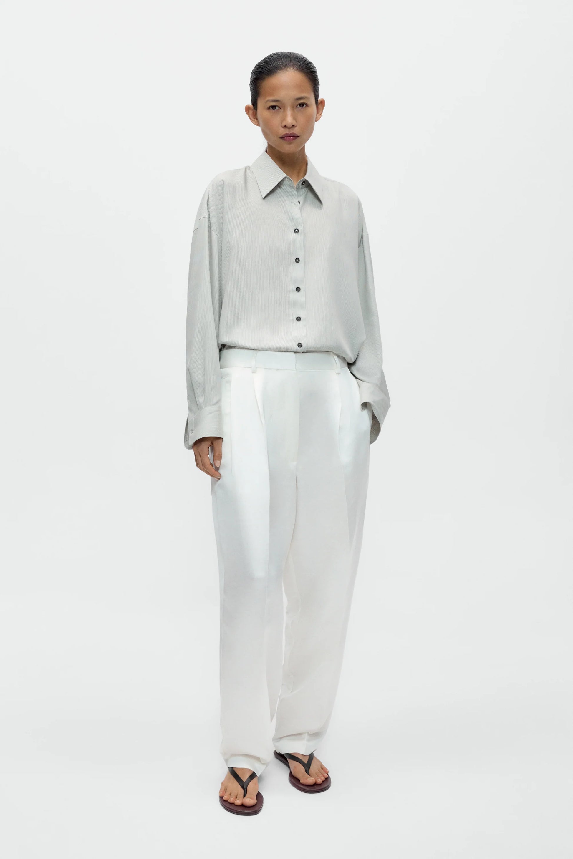 Woman wearing a light gray shirt and white pants on a white background