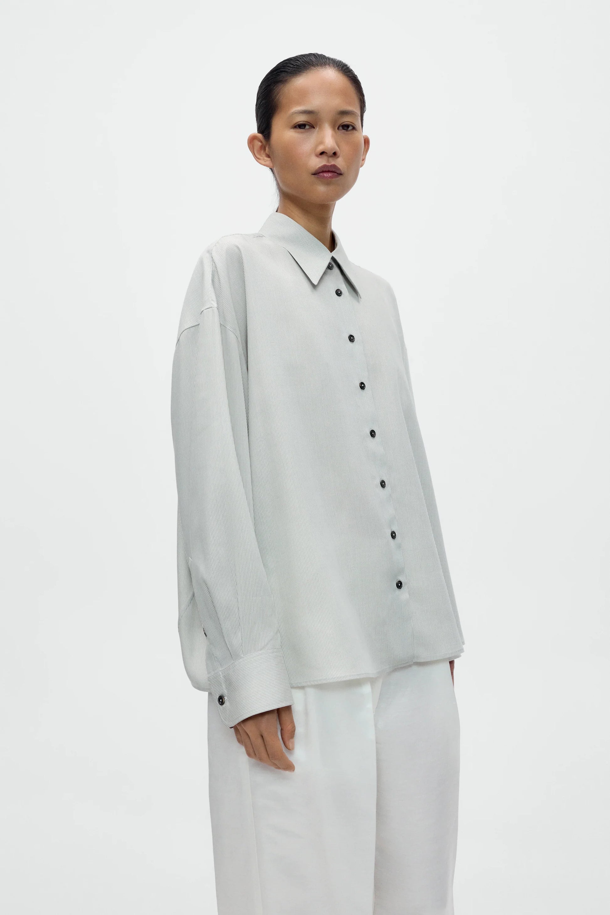 Person wearing a light gray button-up shirt and white pants on a plain background