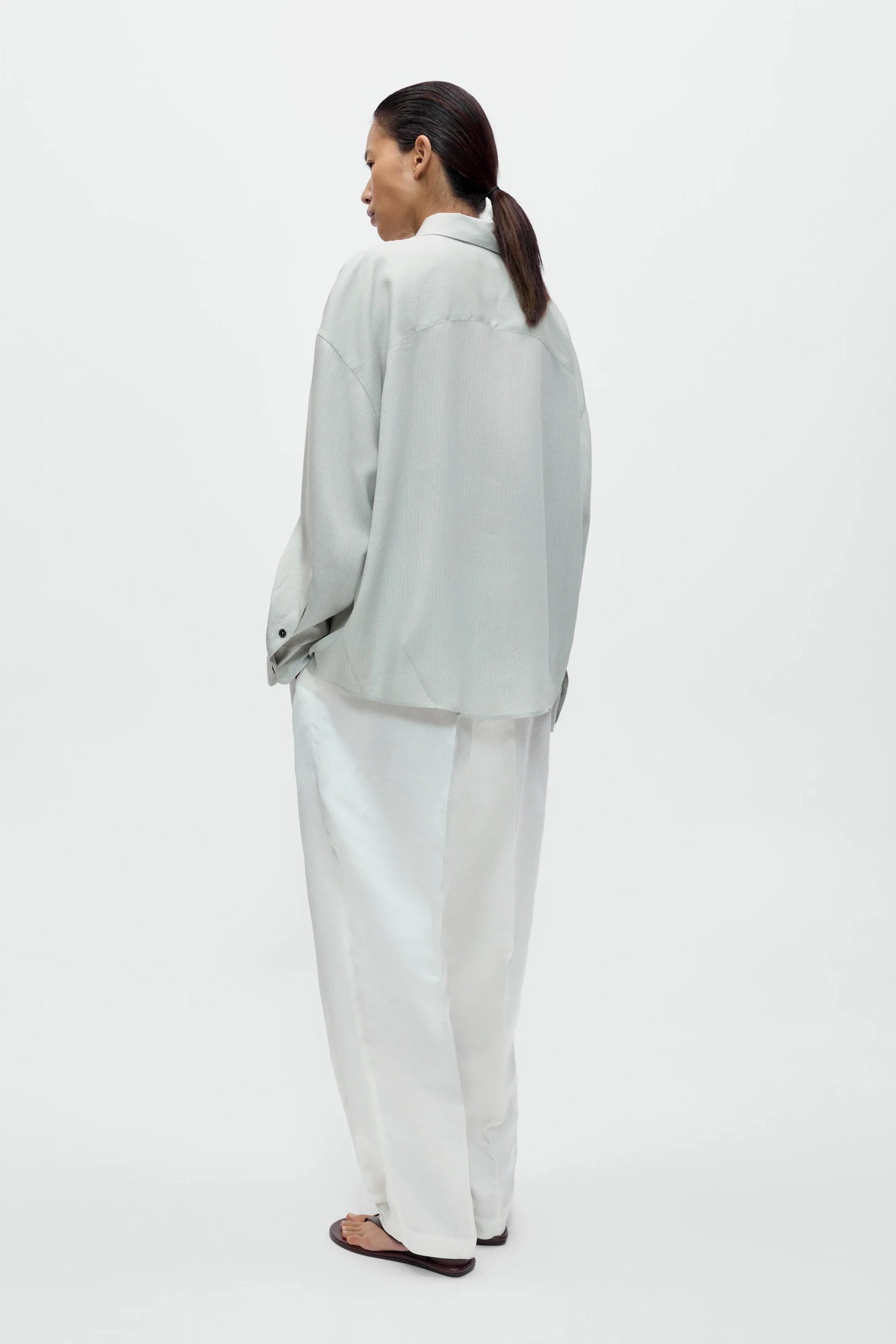 Woman wearing a light gray blazer and white pants on a white background