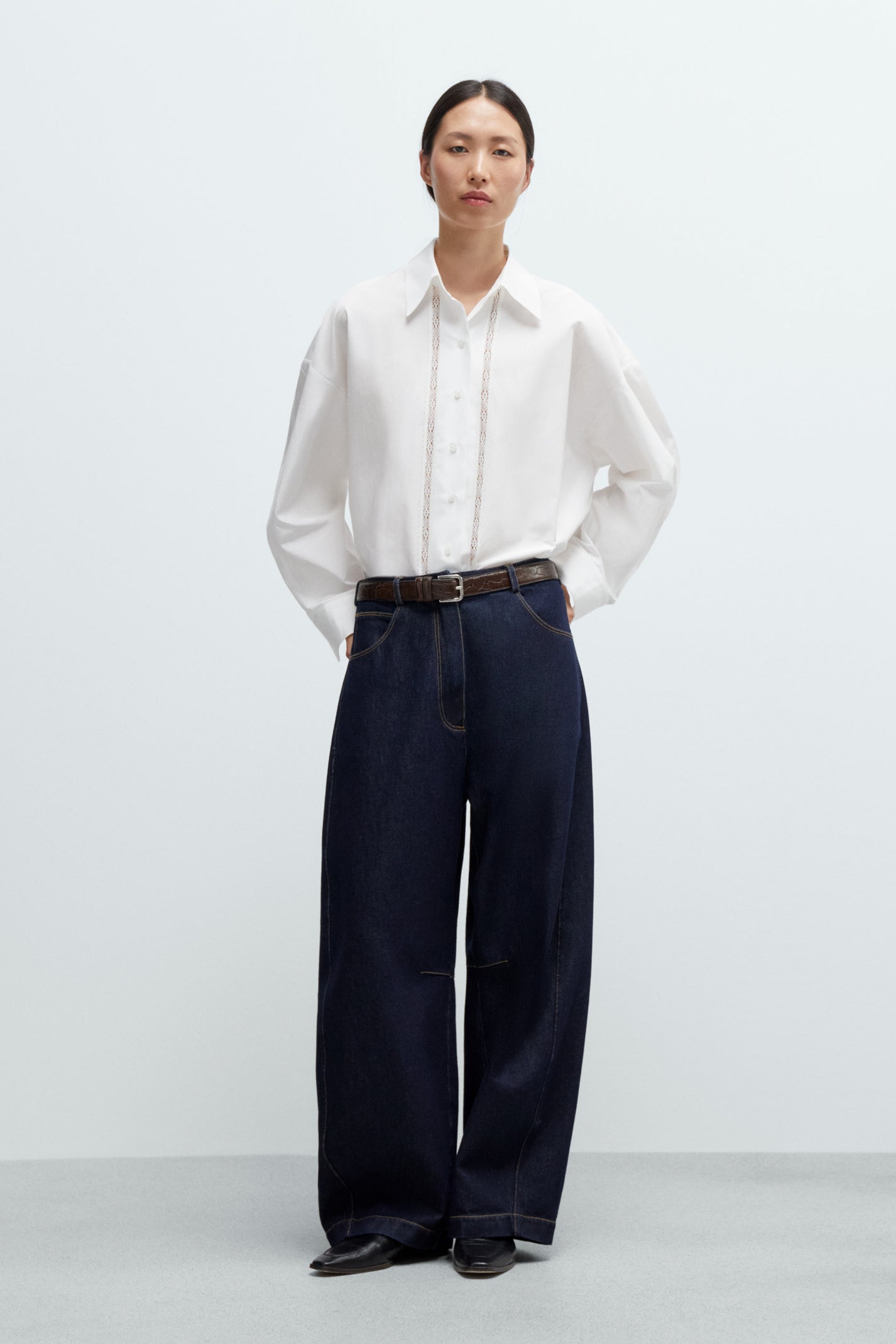 Person wearing a white shirt and dark curved leg baggy Jeans on a white background