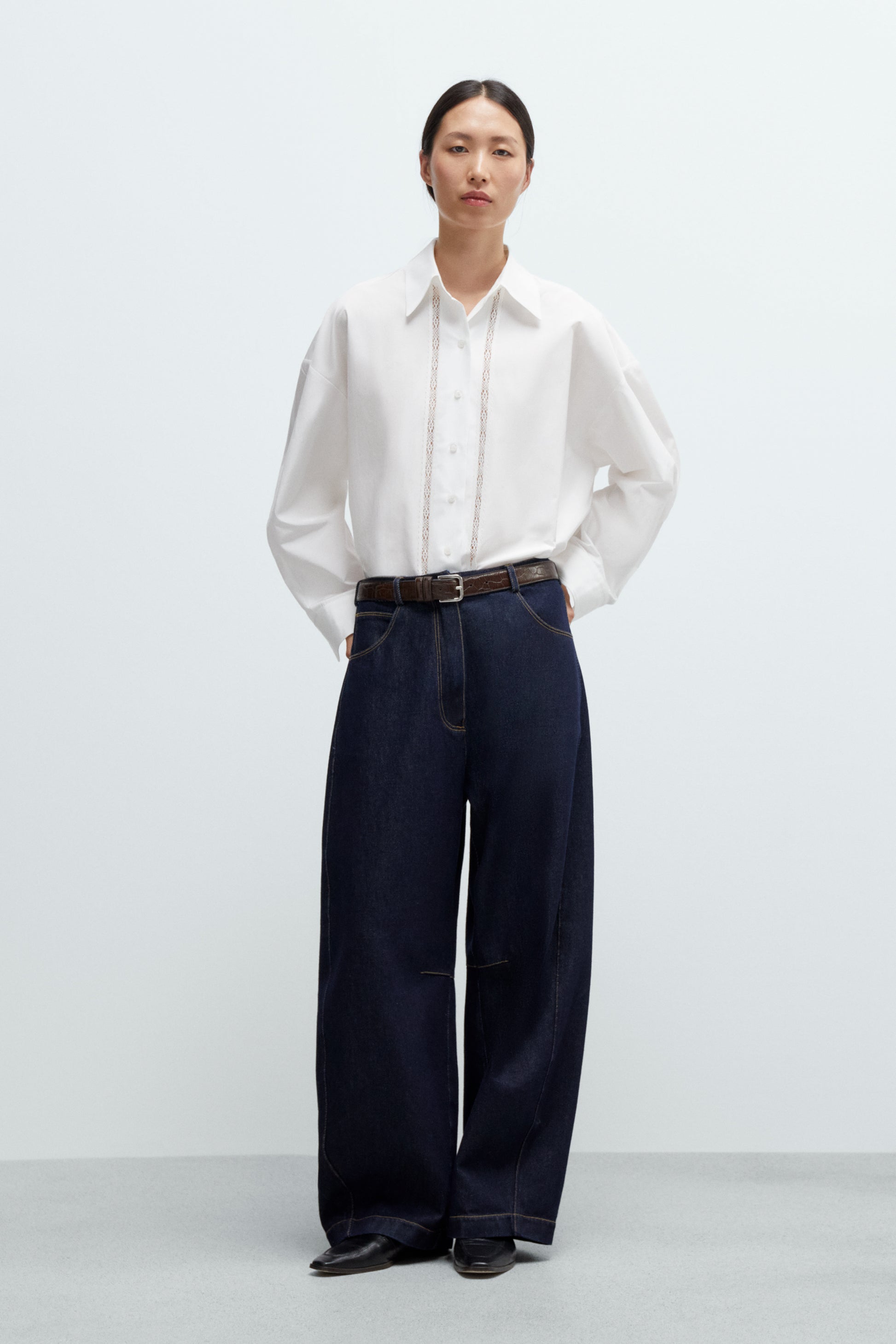 Person wearing a white shirt and dark curved leg baggy Jeans on a white background