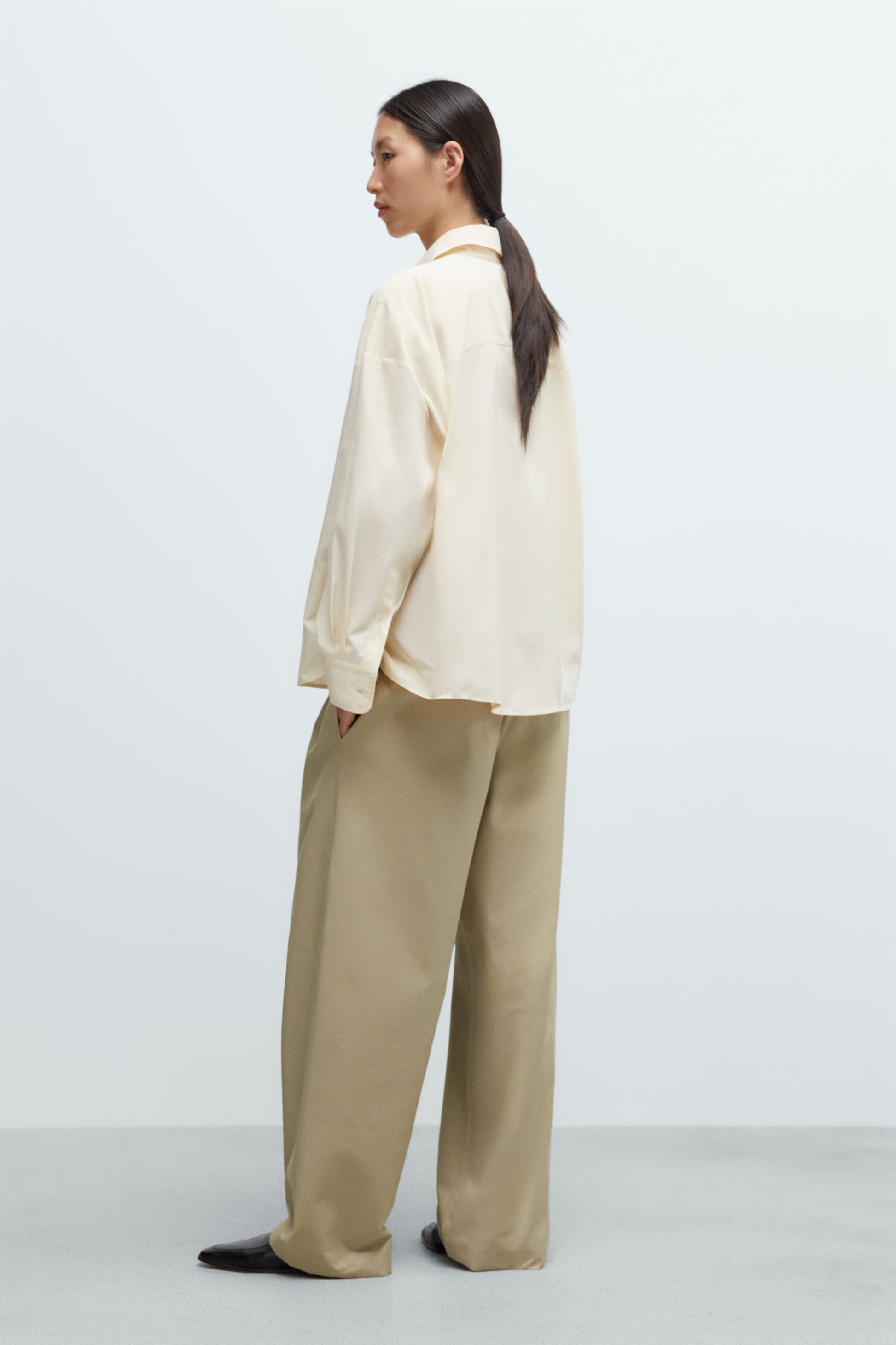 Person wearing a cream blouse and beige pants on a white background