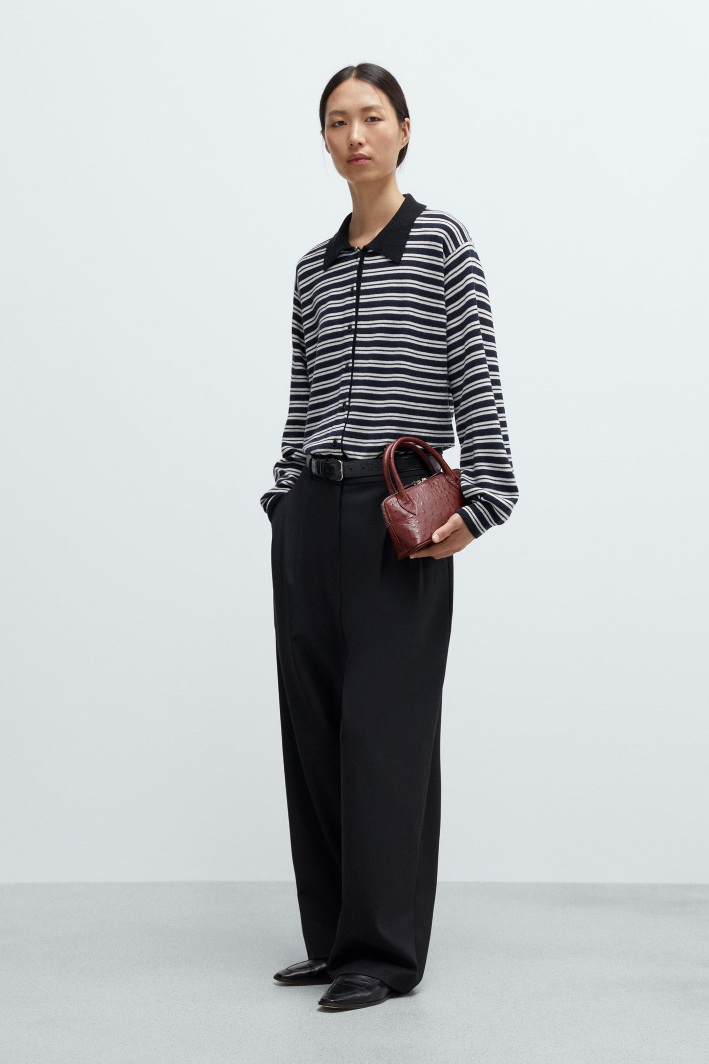 Women wearing a black and white striped cardigan with black pants and holding a brown handbag on a white background