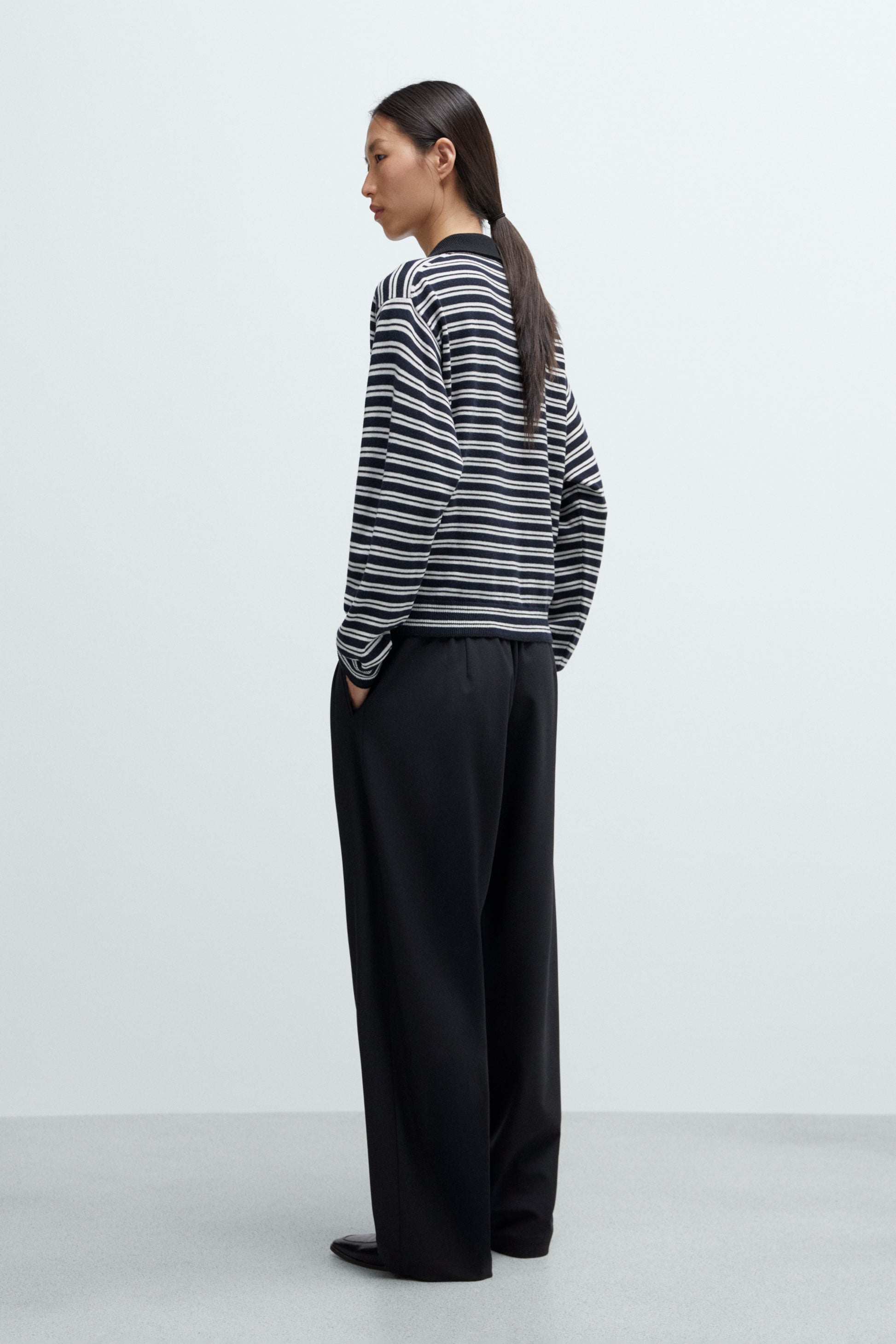 Person wearing a striped sweater and black pants on a white background, viewed from the back.