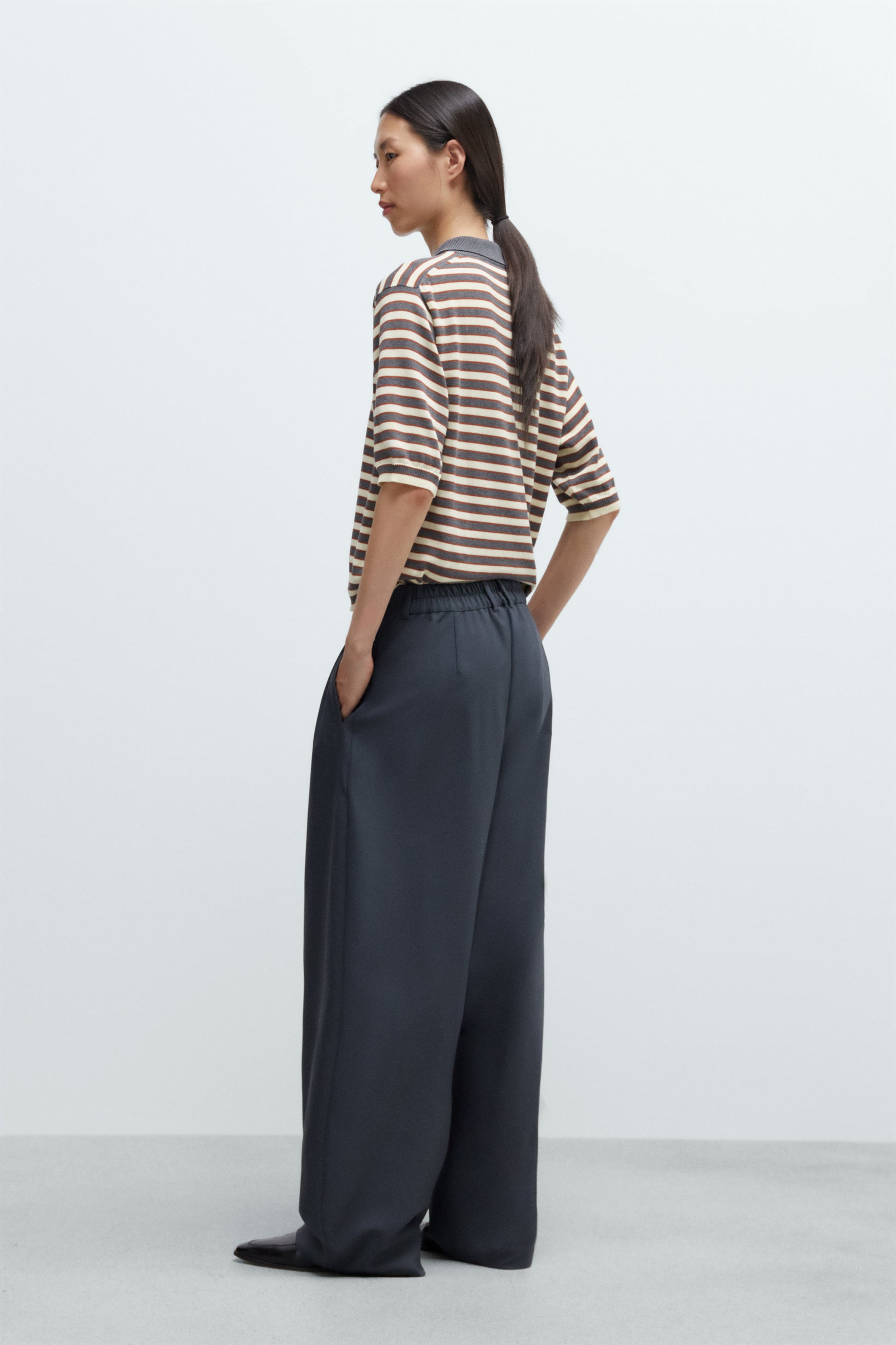 Woman wearing a striped shirt and wide-leg pants against a white background
