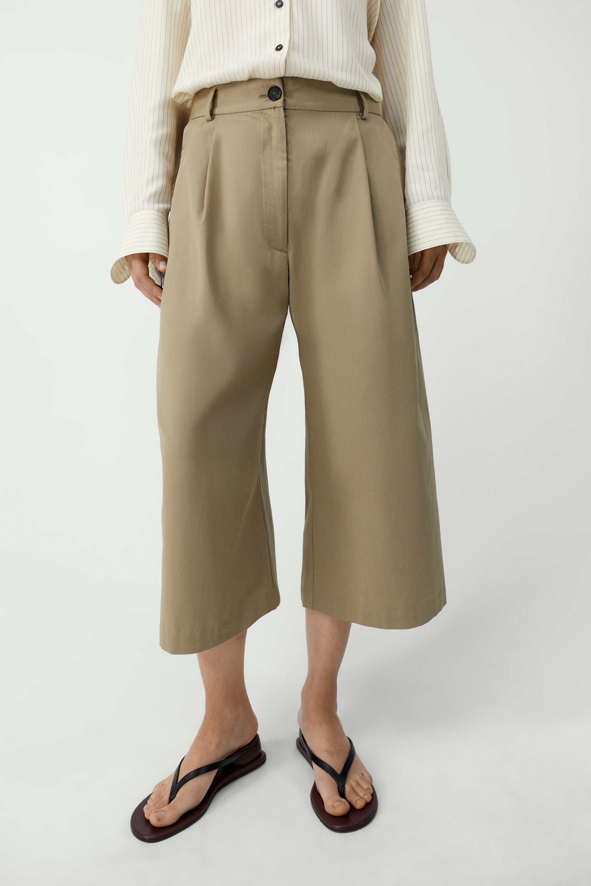 Person wearing beige wide-leg pants on a white background
