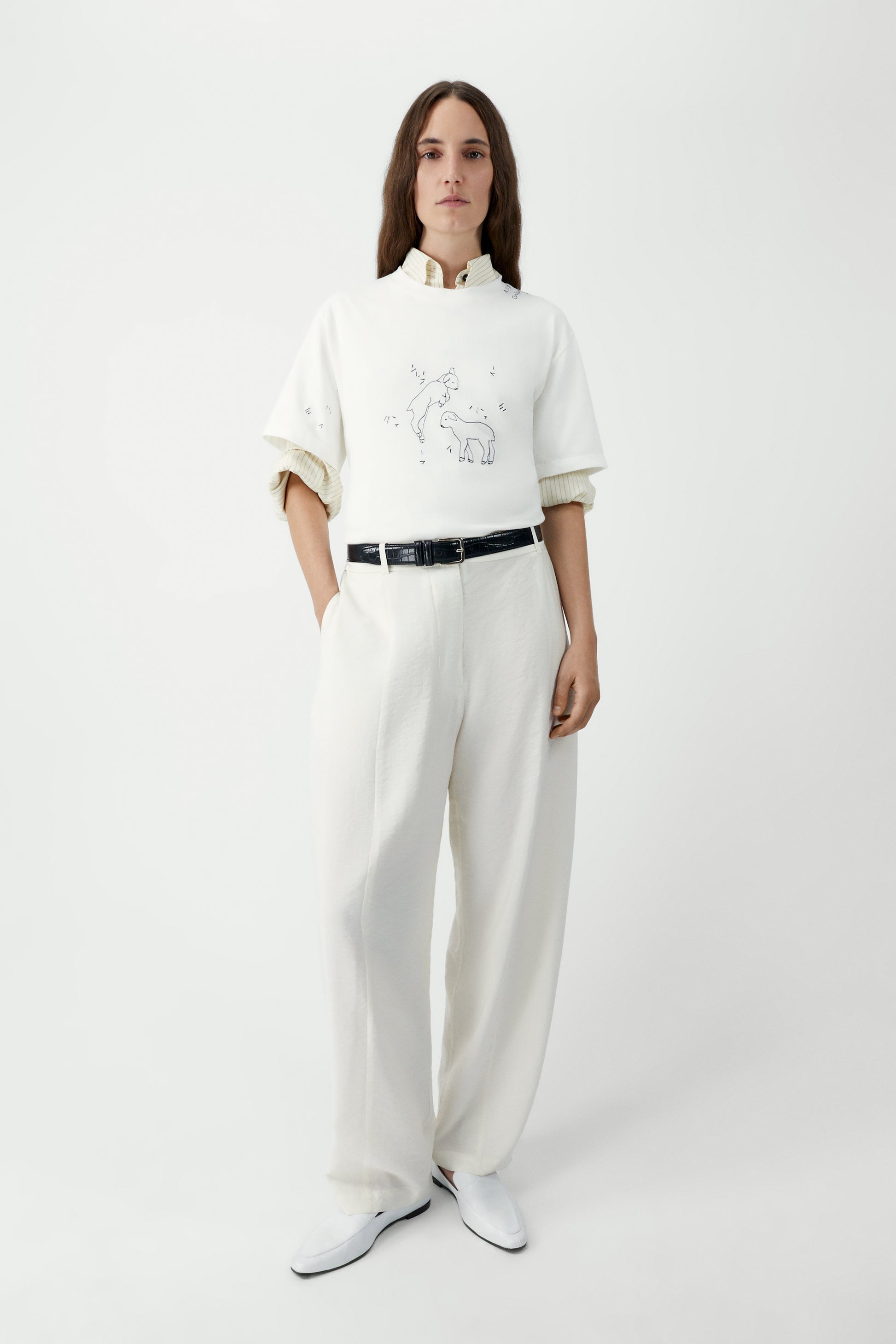 Person wearing a white embroidered t-shirt and white pants on a white background