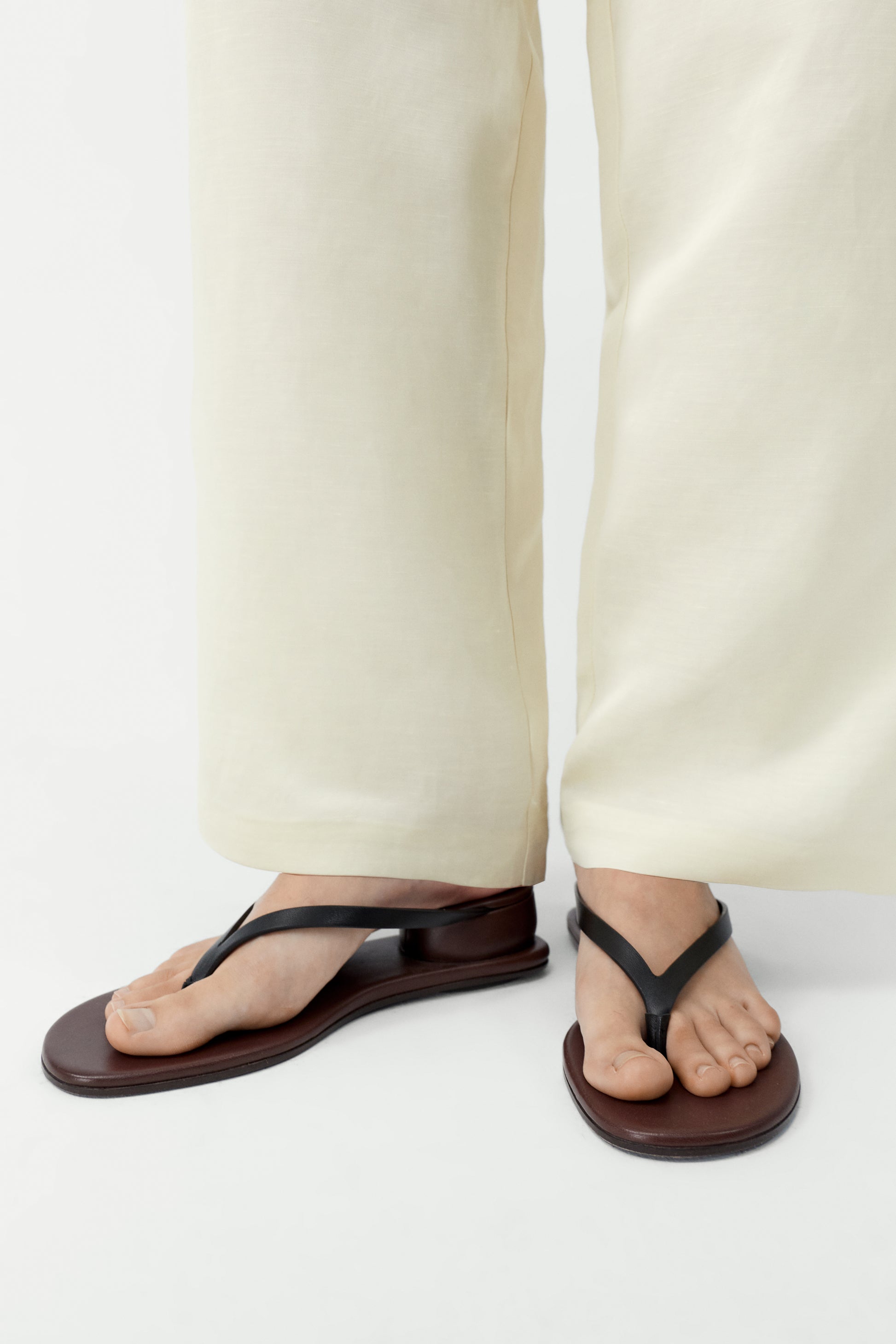 Person wearing black sandals with white pants on a white background