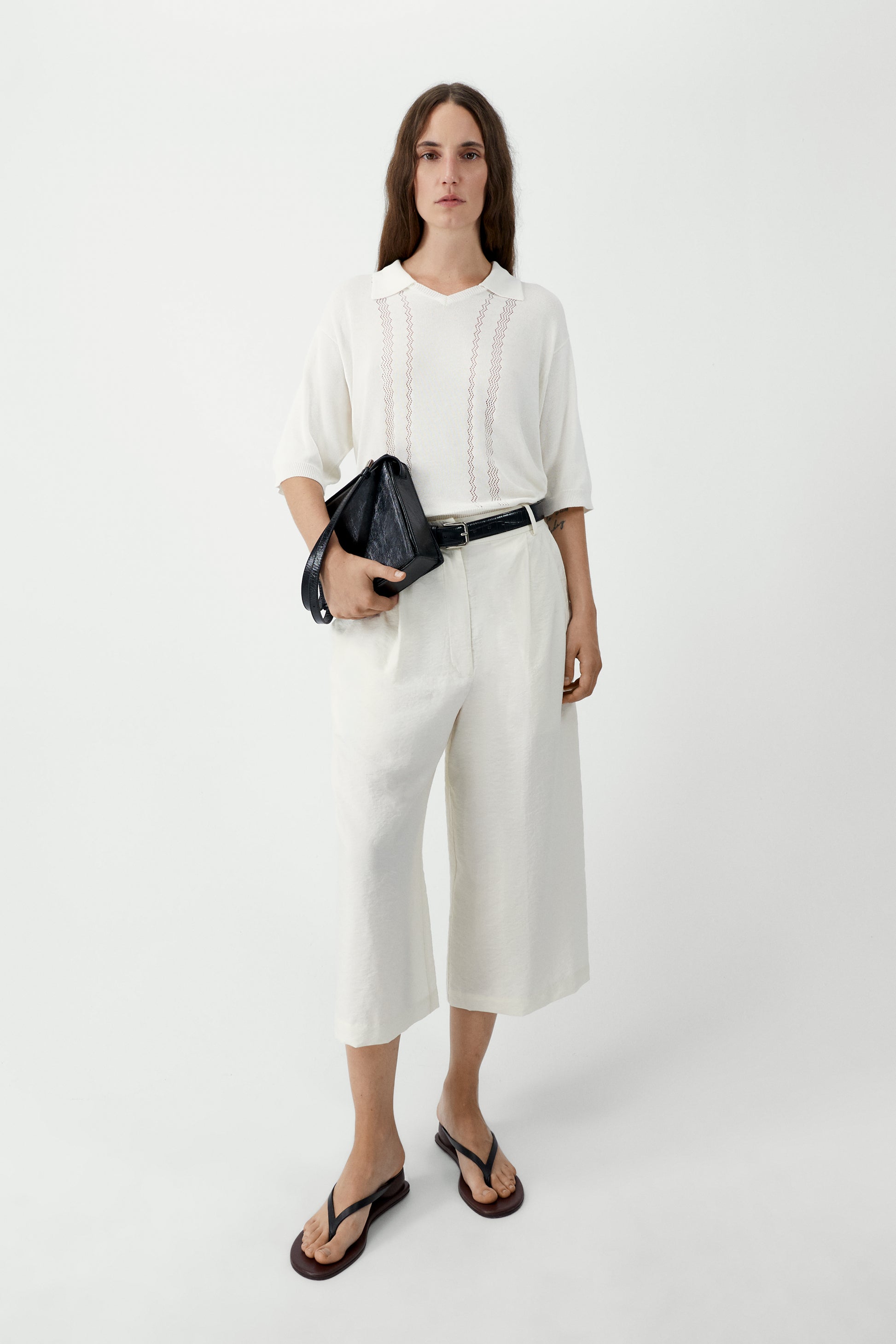 Woman wearing a white outfit with a black bag on a white background