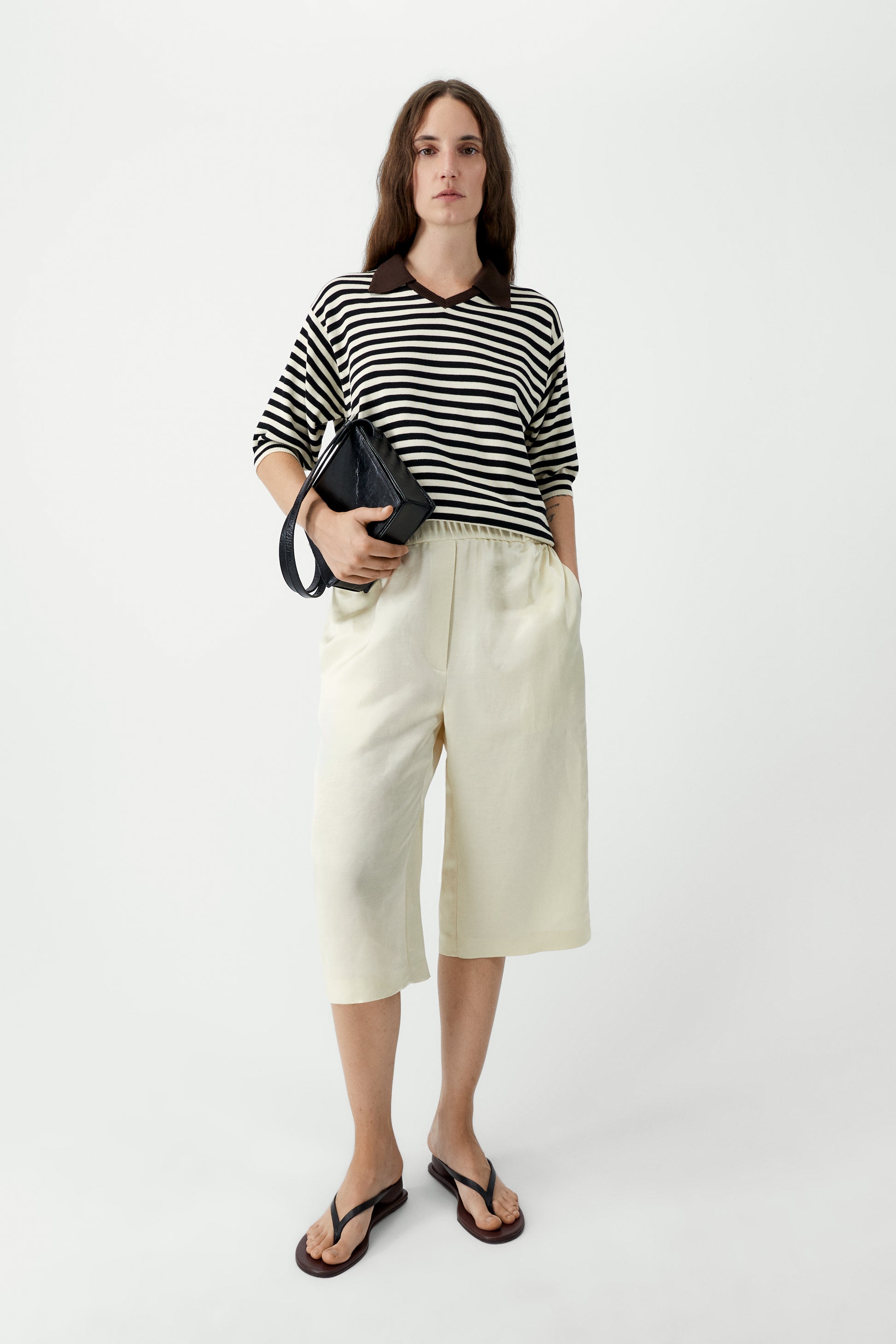 Woman wearing a black and white striped shirt with cream-colored pants on a white background