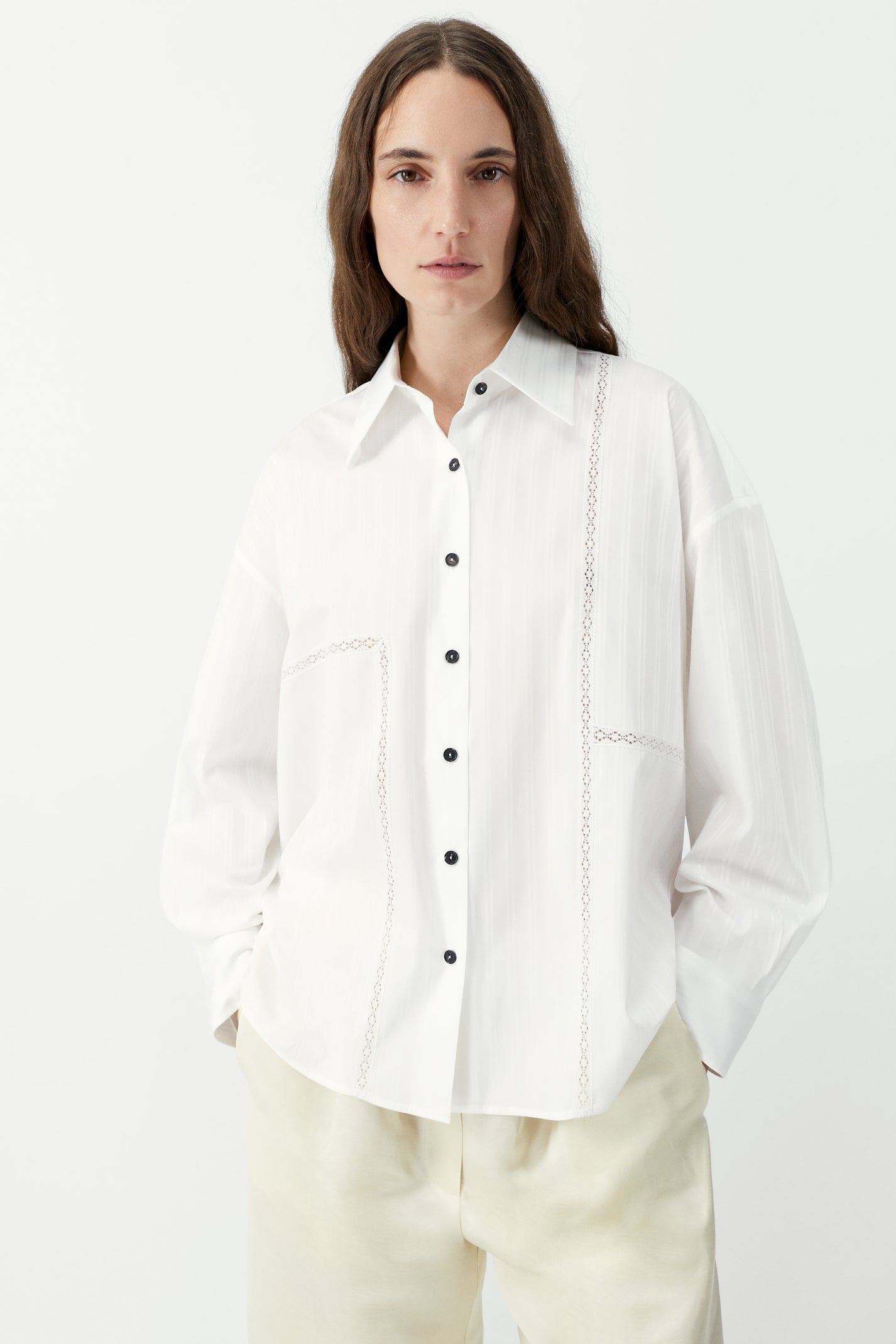 Woman wearing a white shirt with black buttons on a plain background