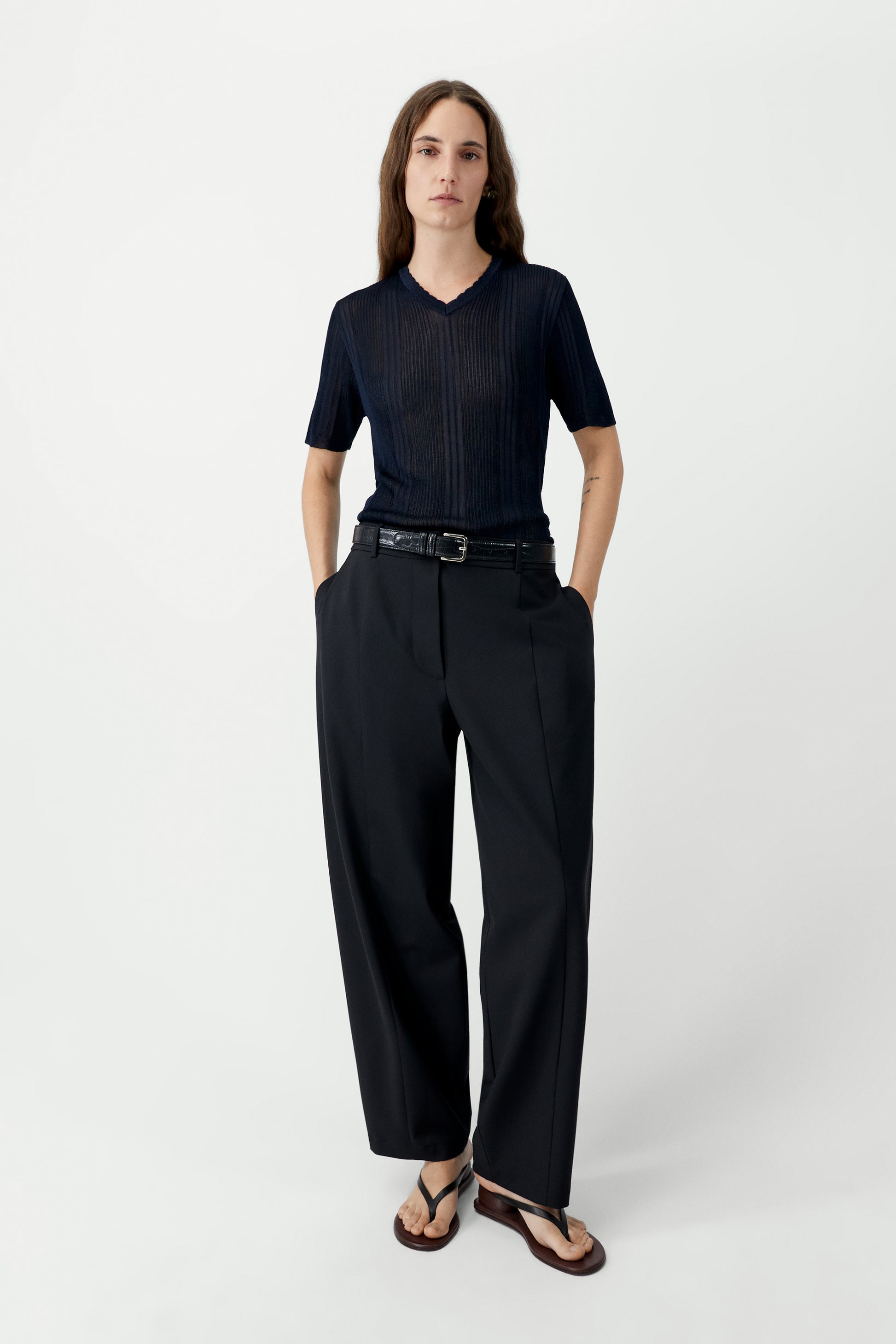 Person wearing a navy short sleeve knitted top with black pants and a belt on a white background