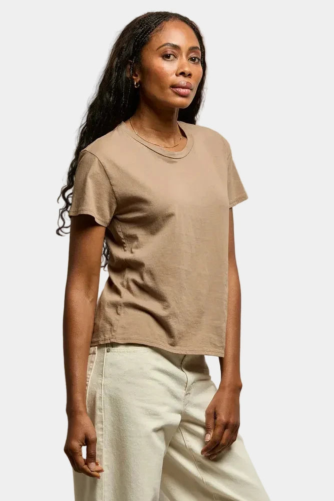 Woman wearing a beige t-shirt and light-colored pants against a neutral background