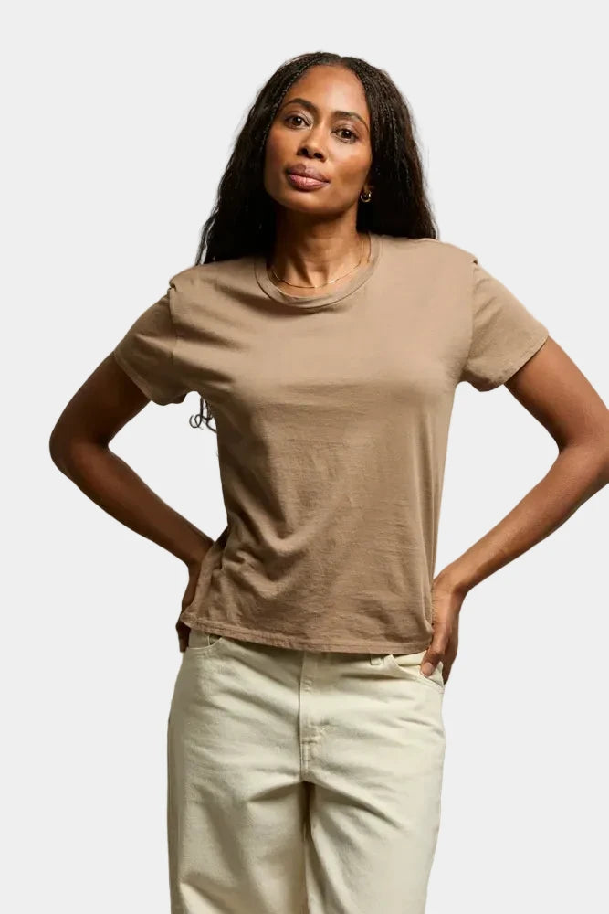 Woman wearing a beige t-shirt and light-colored pants against a plain background
