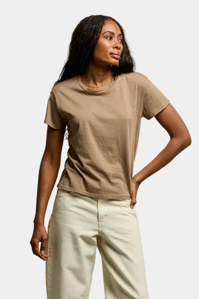 Woman wearing a beige t-shirt and light-colored pants against a neutral background